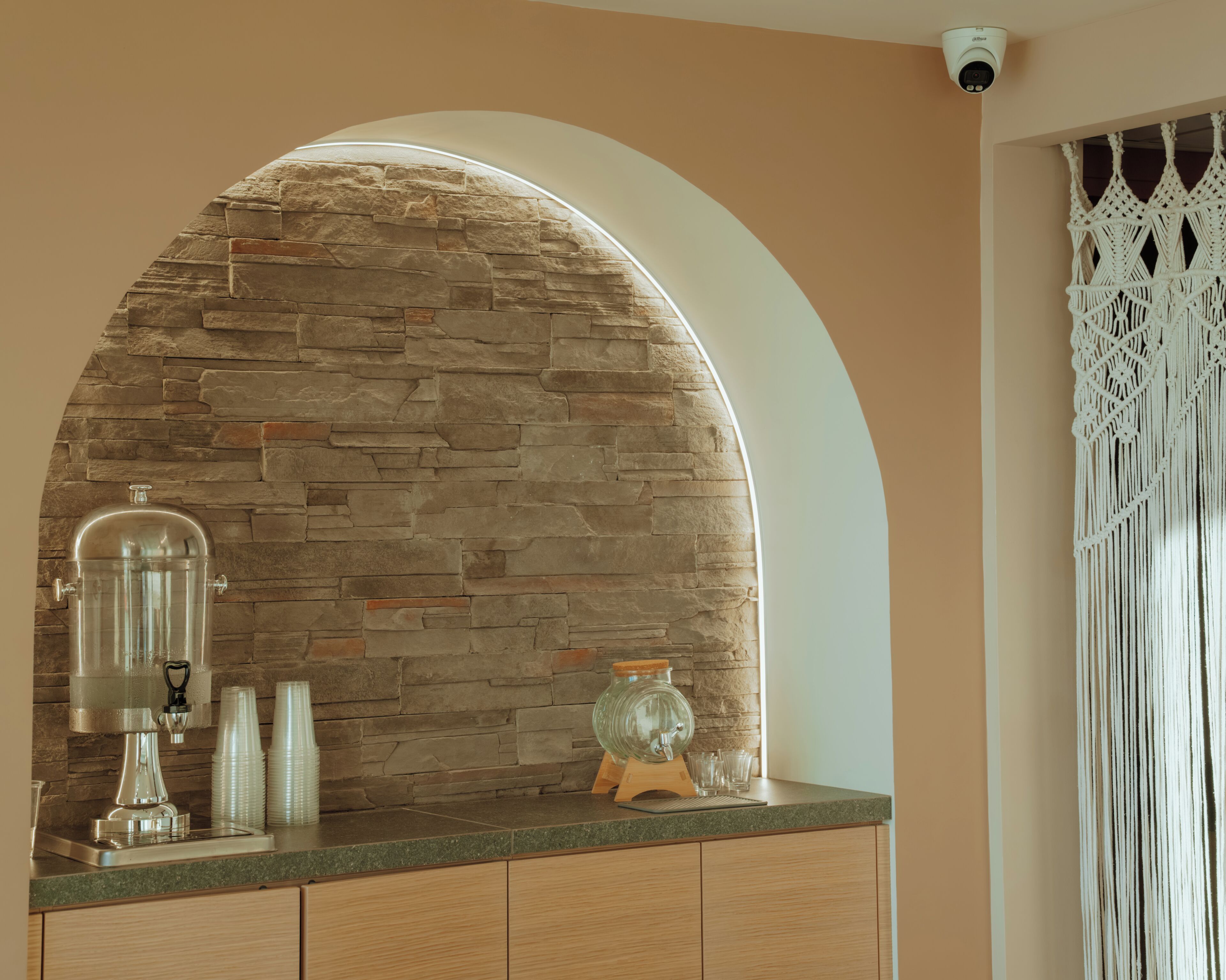 A kitchen with a stone wall, a coffee machine, and a macrame curtain.