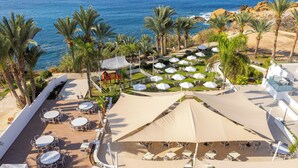 A resort with outdoor seating areas, palm trees, and a view of the ocean. - Queen's Bay Hotel (Kissonerga)