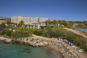 A coastal hotel with a beach area, palm trees, and a rocky shoreline. - Queen's Bay Hotel (Kissonerga)