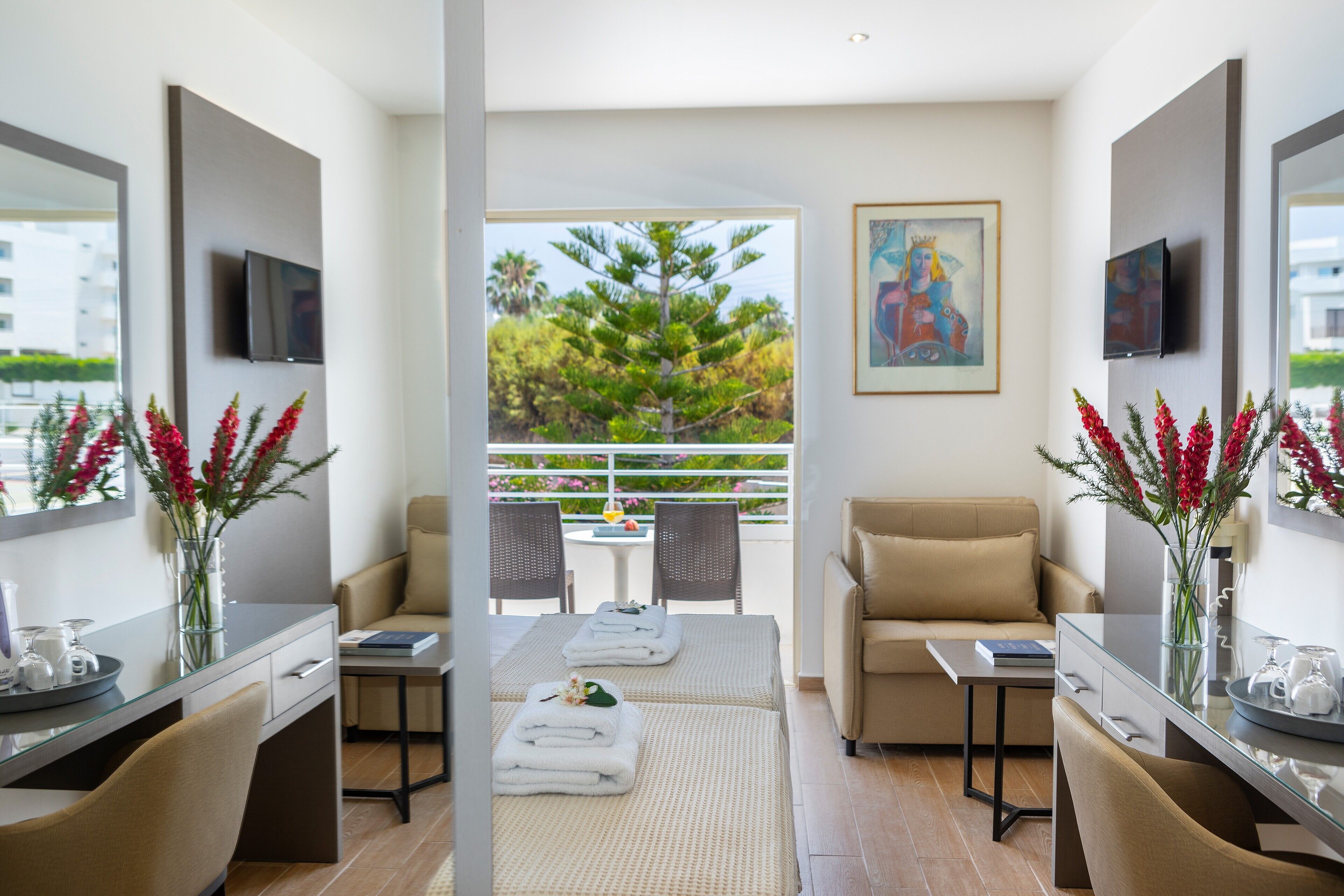 A modern hotel room with a balcony, a sofa, a dining table, and a TV mounted on the wall.