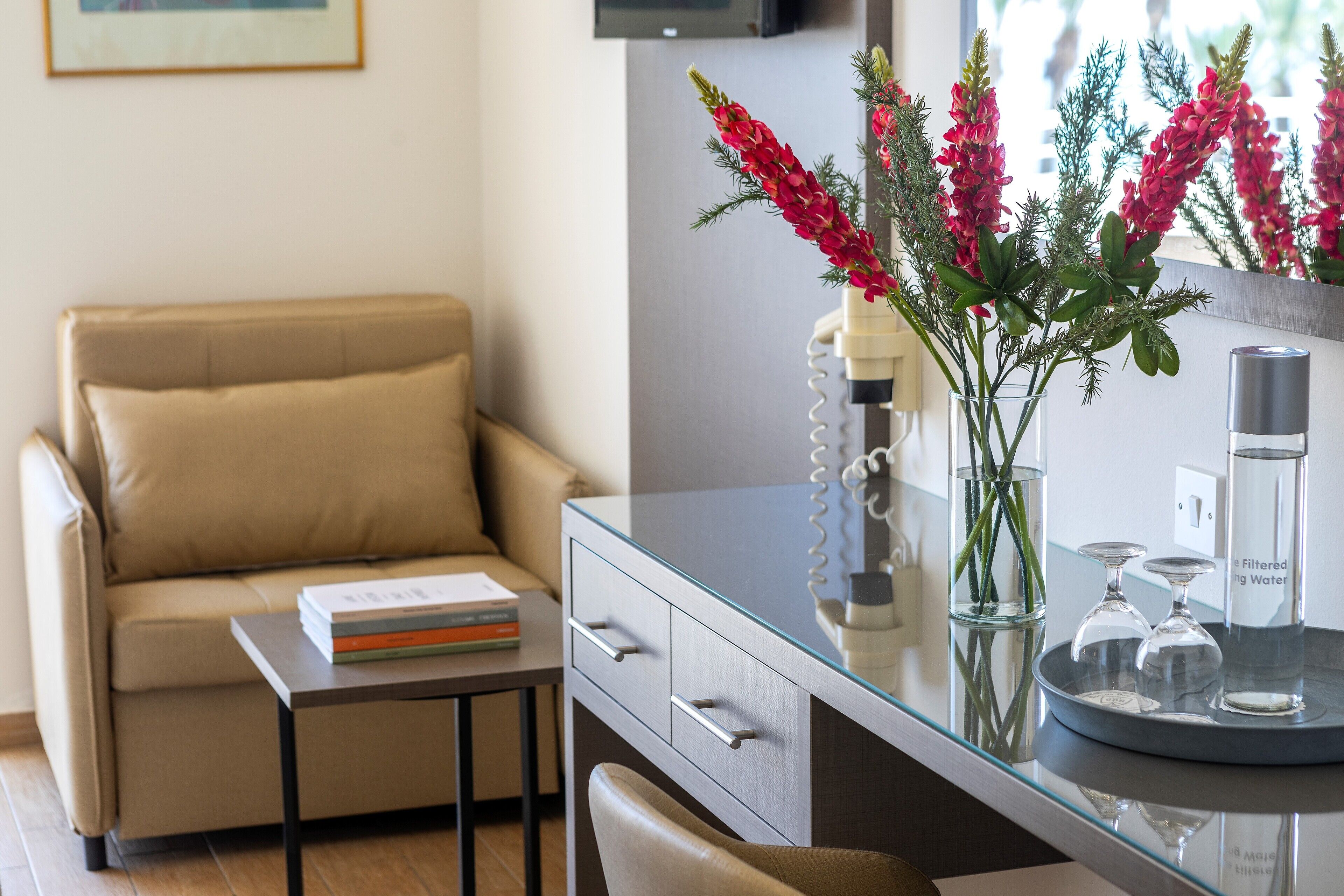 A modern living room with a beige sofa, a glass coffee table, and a glass cabinet with decorative items.