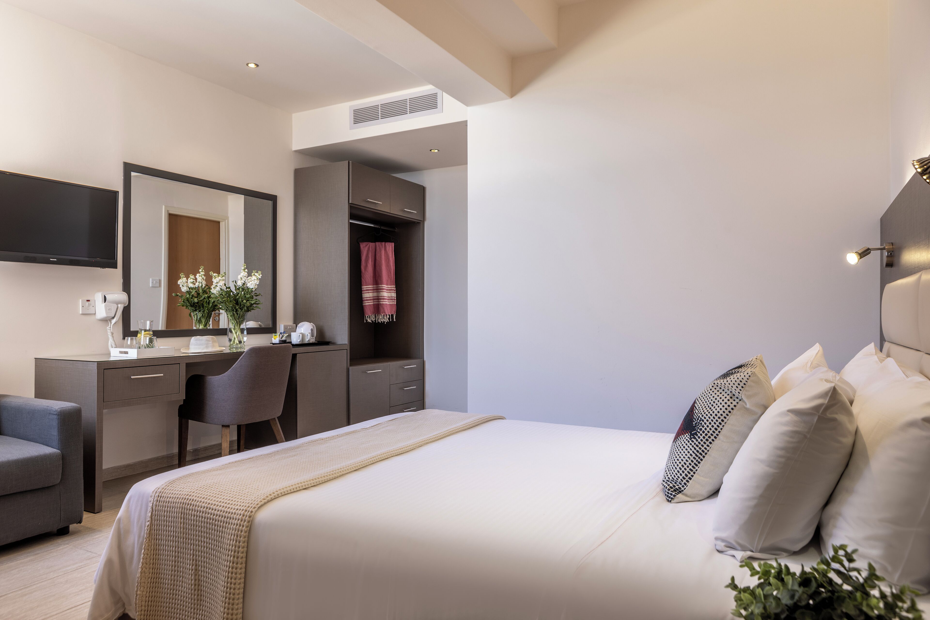 A modern hotel room with a bed, a desk, a chair, a wardrobe, and a large mirror.