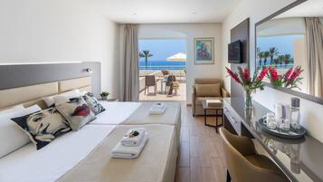 Een hotelkamer met een bed, een bank, een televisie en uitzicht op het strand.