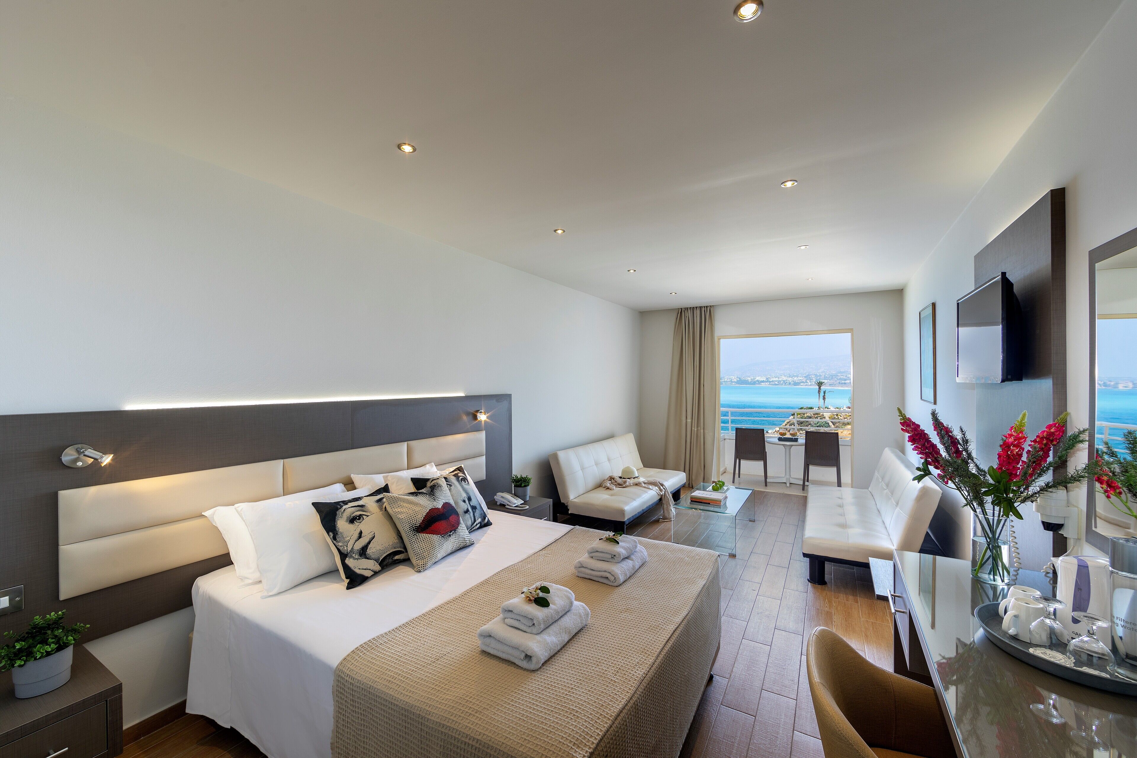Ein modernes Hotelzimmer mit einem großen Bett, einer Sitzecke, einem Essbereich und Blick auf das Meer.
