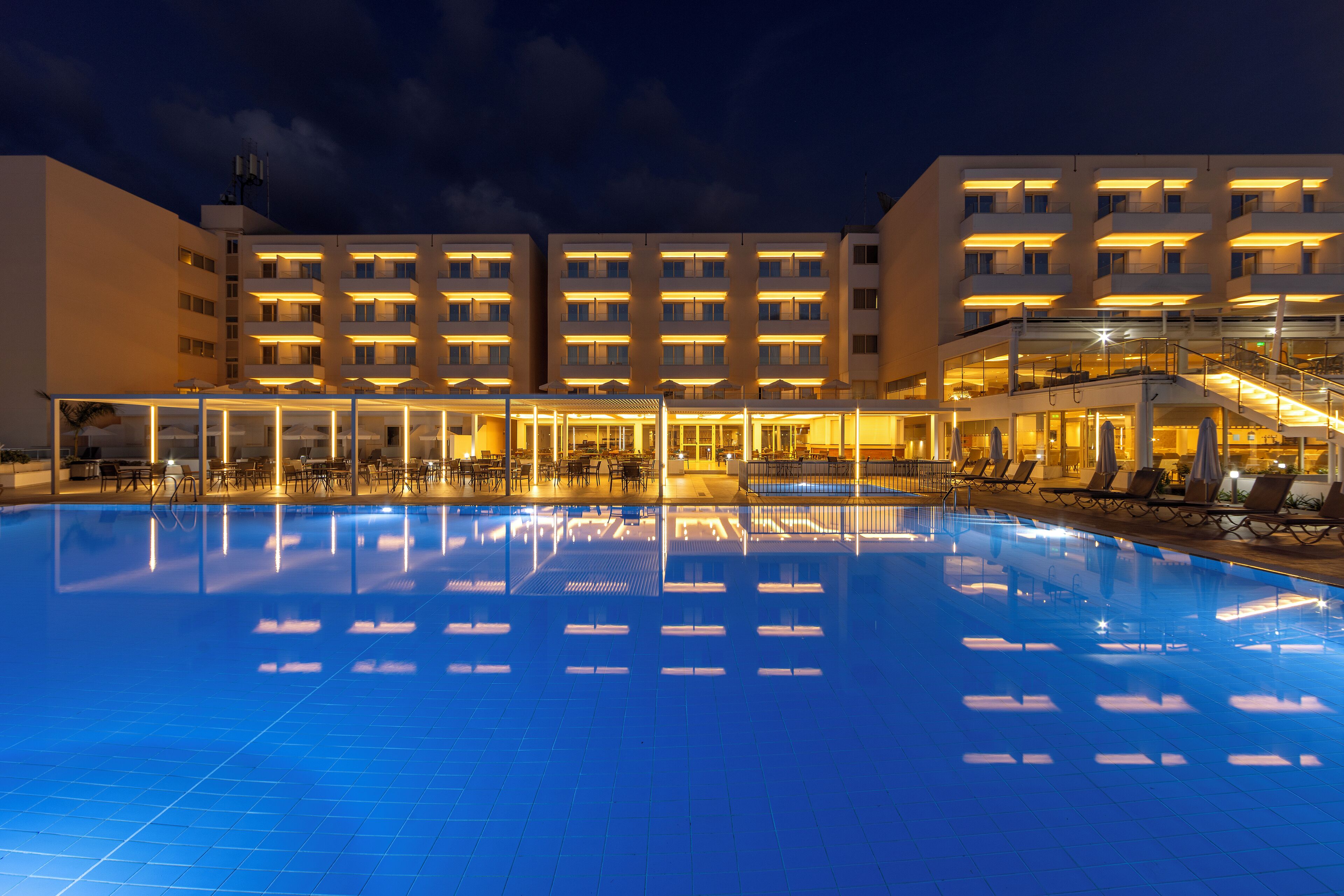 A hotel with a swimming pool, outdoor seating, and a well-lit building facade.