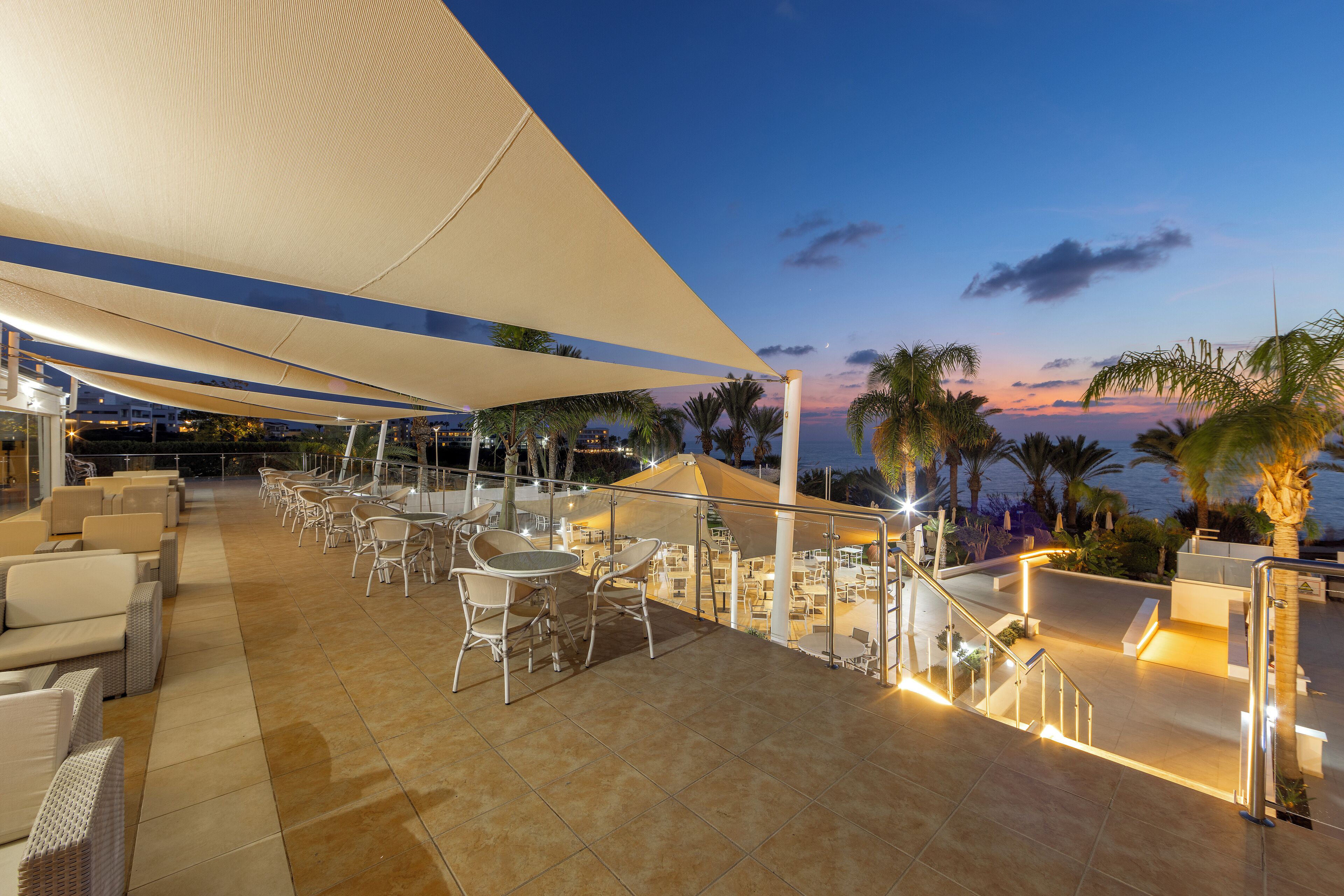 Terraza al aire libre con asientos y mesas, con vista a un cuerpo de agua al atardecer.