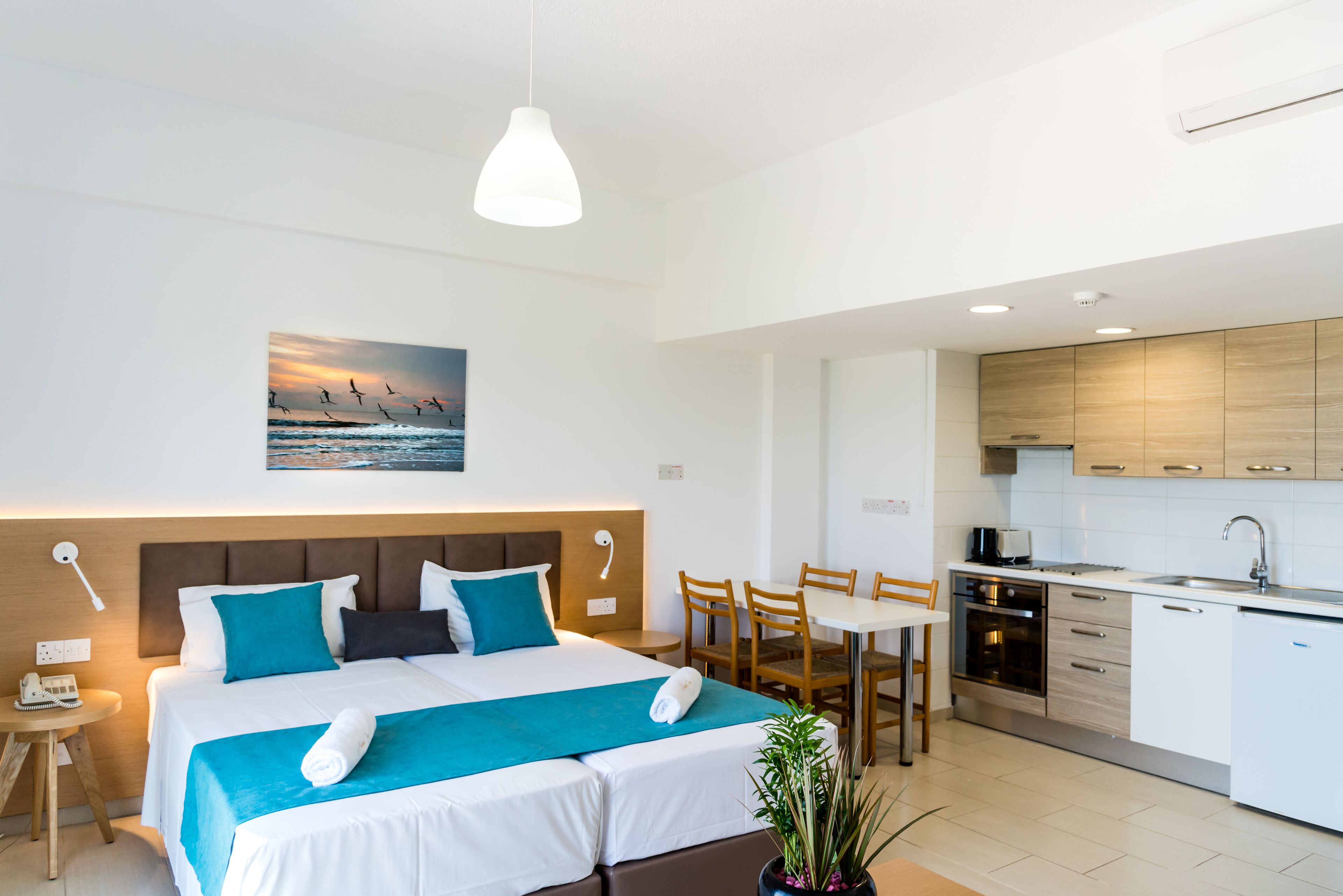 A modern hotel room with a large bed, a dining area, and a kitchenette.