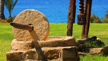 A stone mill wheel and wooden mill components on a grassy hill with a view of the ocean.