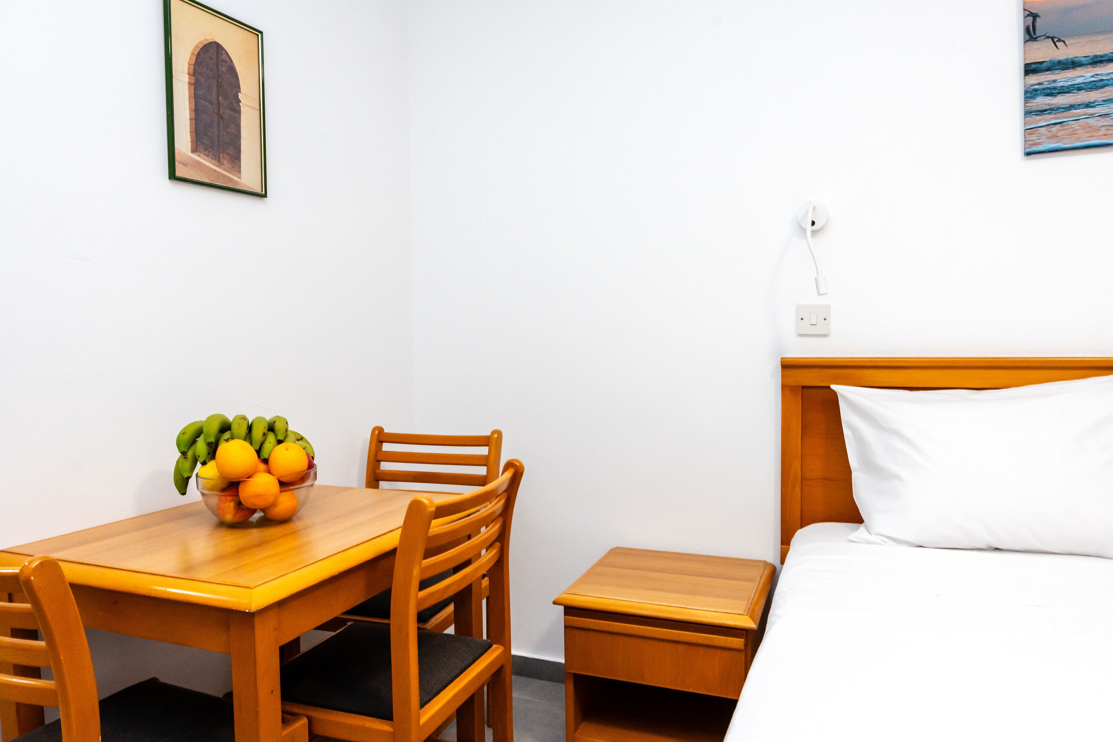 Ein Hotelzimmer mit einem hölzernen Bett, einem kleinen Nachttisch, einem Holztisch mit Stühlen und einer Obstschale auf dem Tisch.