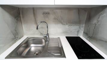 A modern kitchen with a stainless steel sink, a black induction cooktop, and white cabinetry.