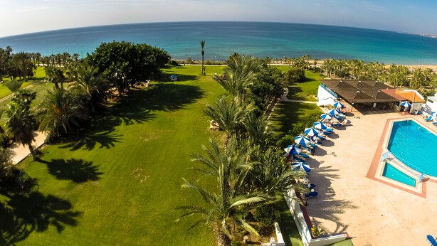 A resort with a pool, palm trees, and a view of the ocean. - Helios Bay Hotel Apartments (Chlorakas)
