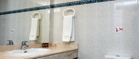 Un baño con lavamanos, espejo, toalleros y retrete.