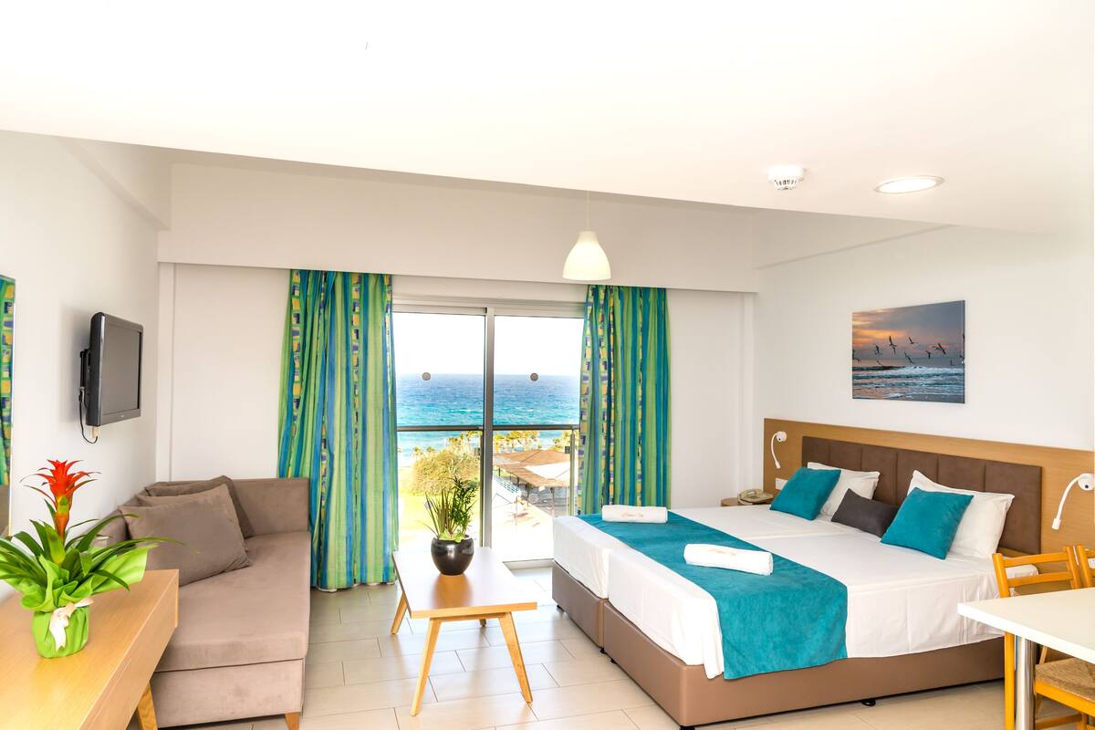 A hotel room with a bed, a sofa, a dining table, and a TV.