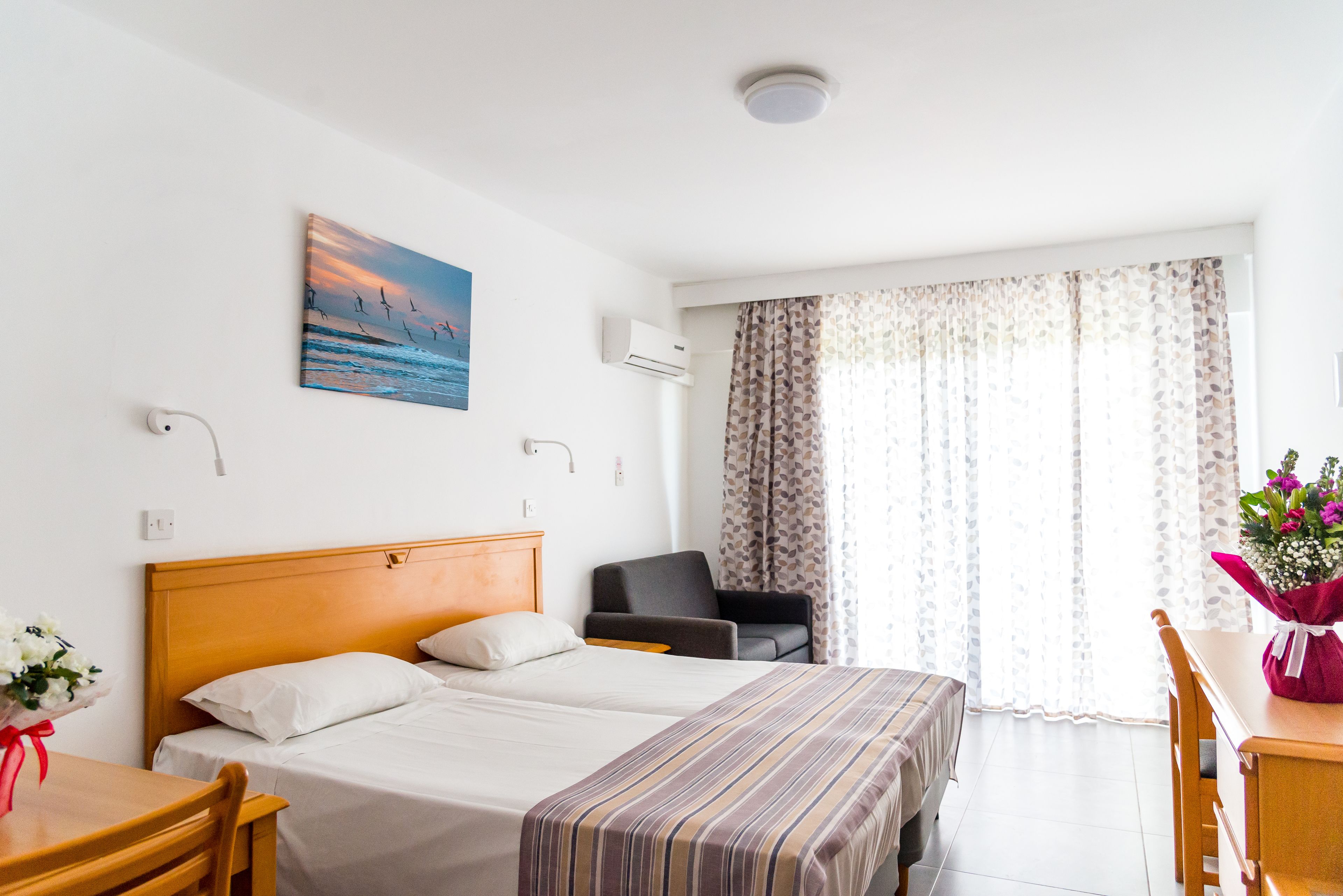 Habitación de hotel con dos camas, un escritorio, una silla, una mesa, un cuadro y una ventana con cortinas.