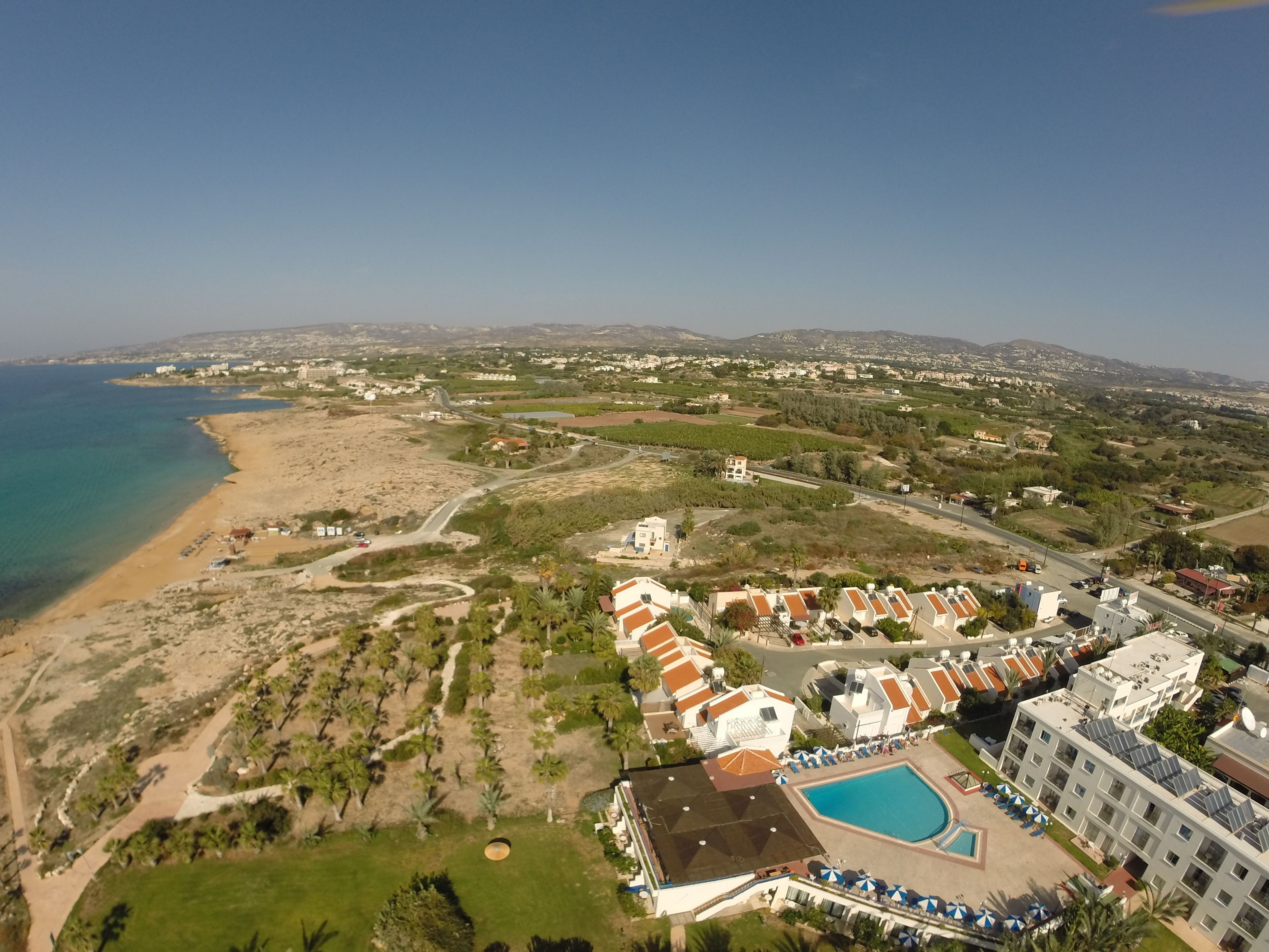 An aerial view of a coastal resort with a swimming pool, beach, and residential buildings.