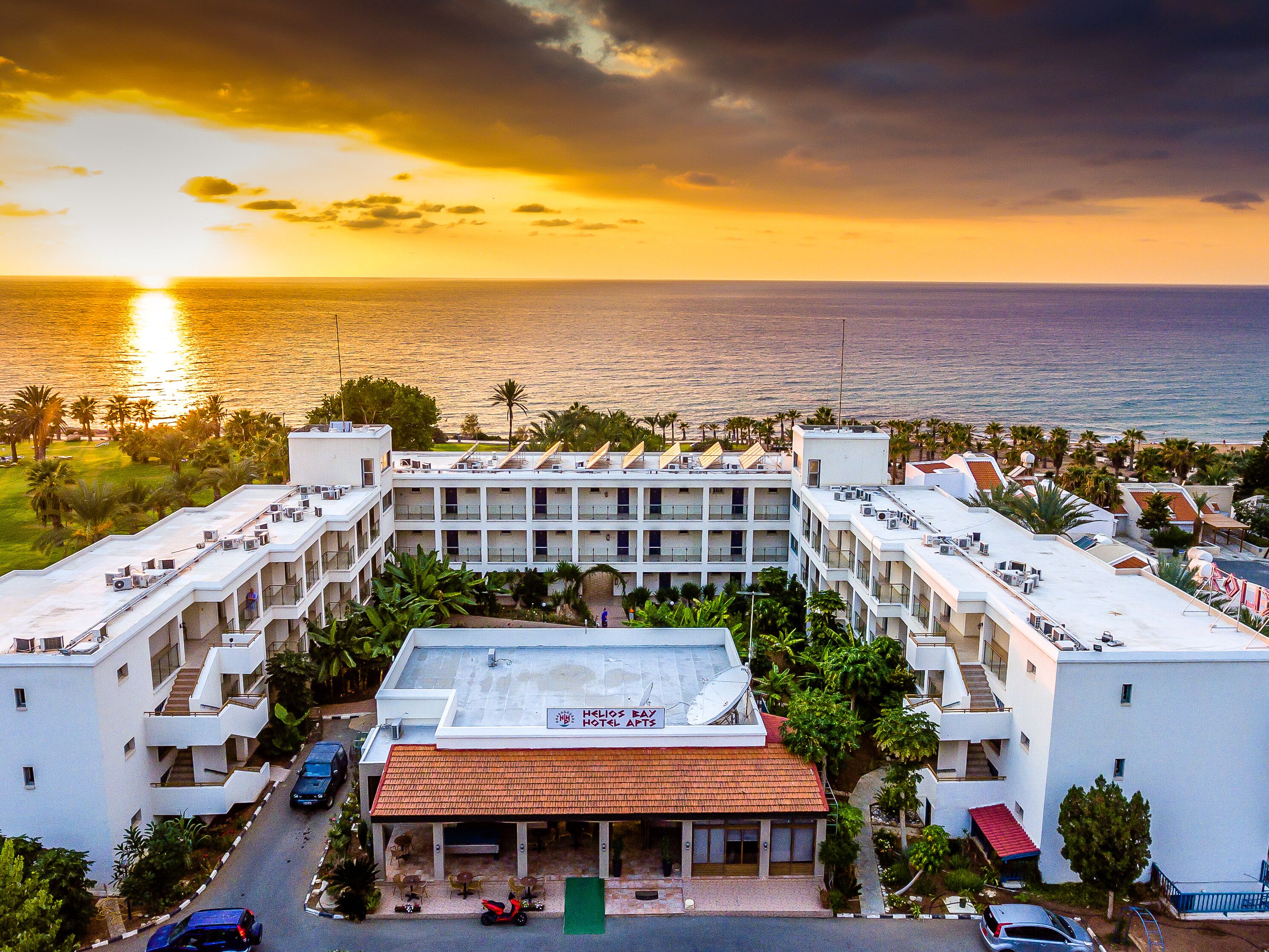A hotel with multiple floors, a rooftop pool, and a view of the sea at sunset.