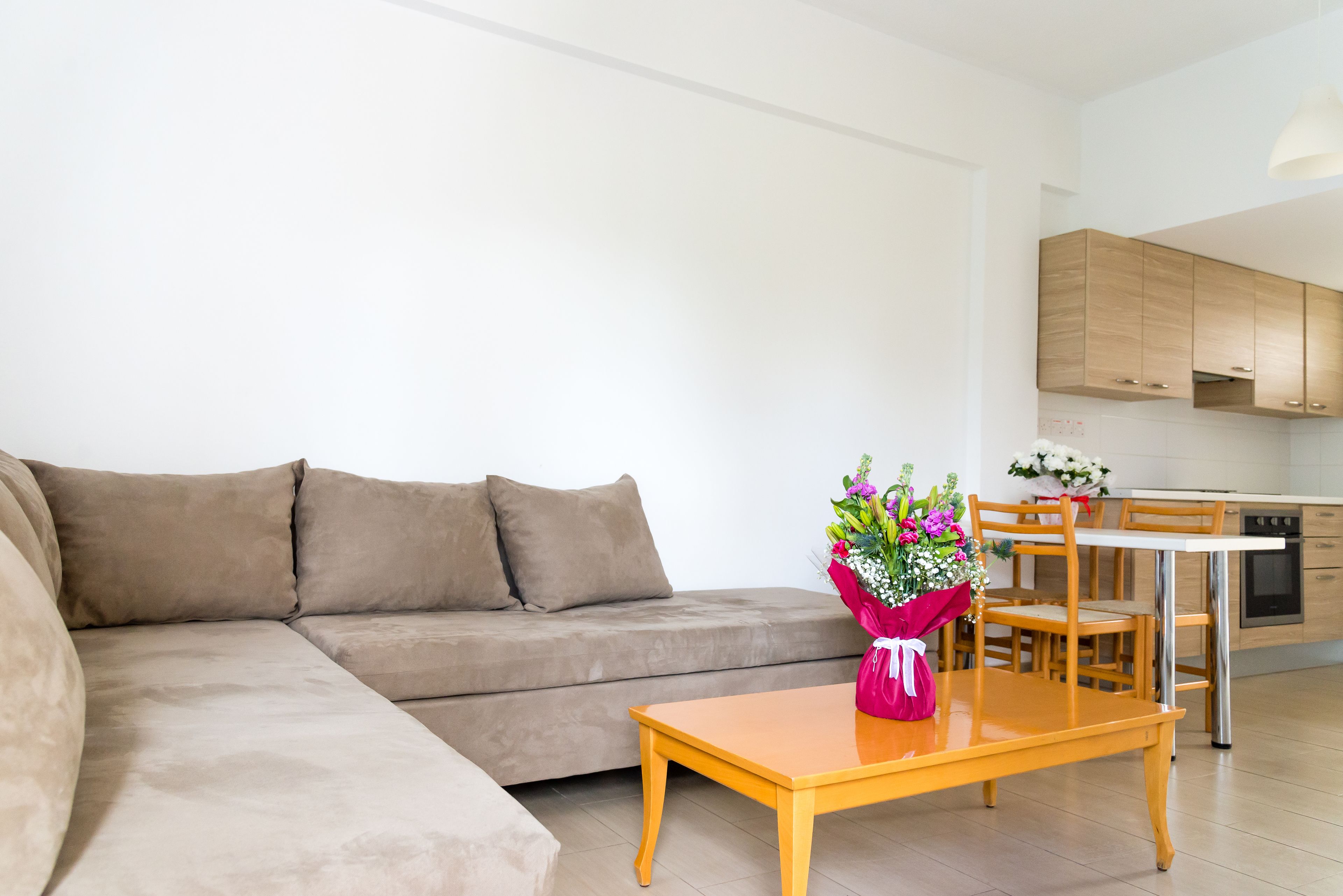Een moderne woonkamer met een beige bank, een houten salontafel en een bloemenboeket.