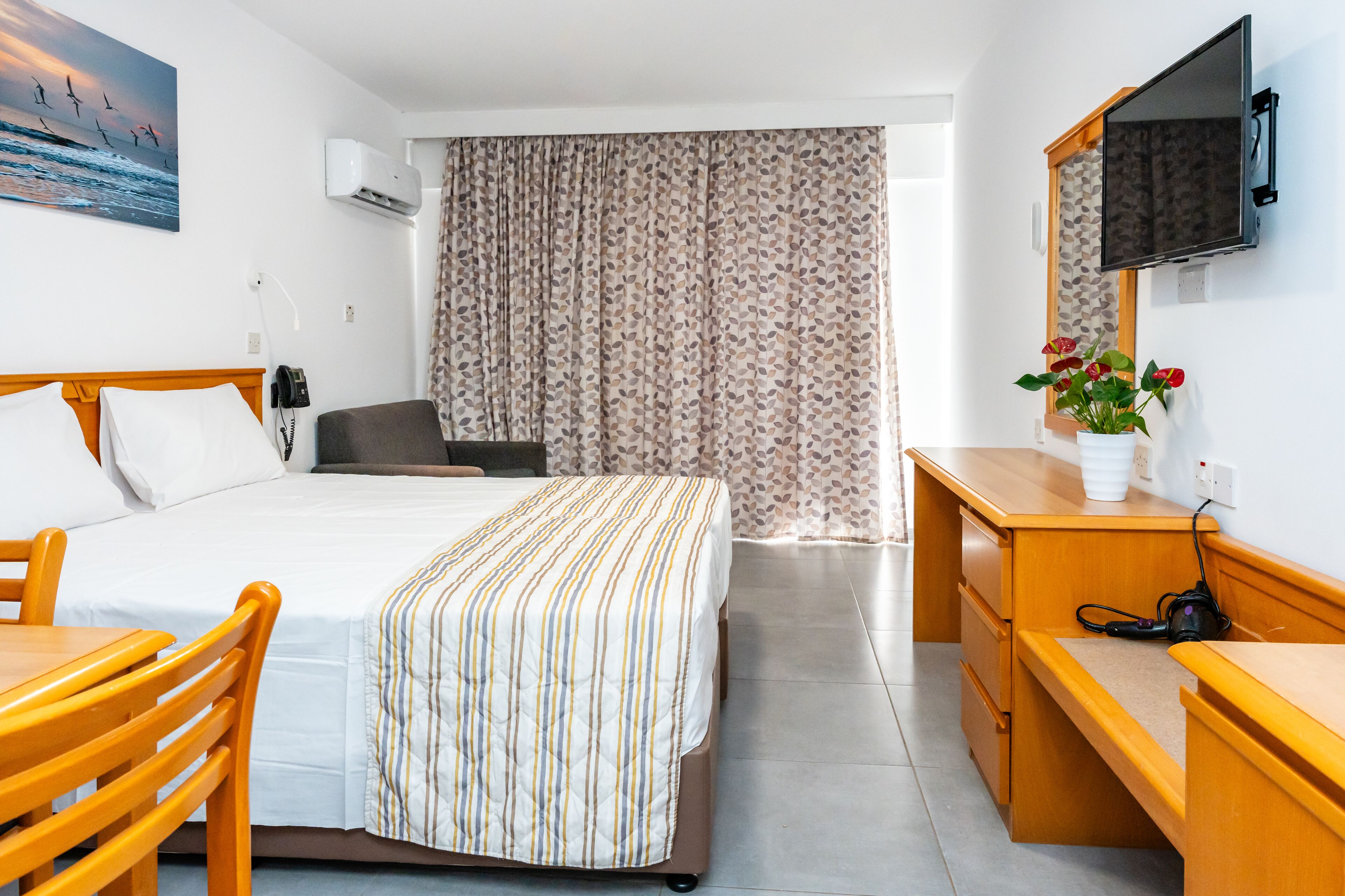 Habitación de hotel con cama, escritorio, silla, televisor y ventana con cortinas.
