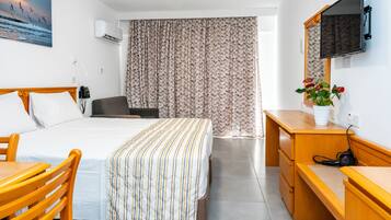 Habitación de hotel con cama, escritorio, silla, televisor y ventana con cortinas.