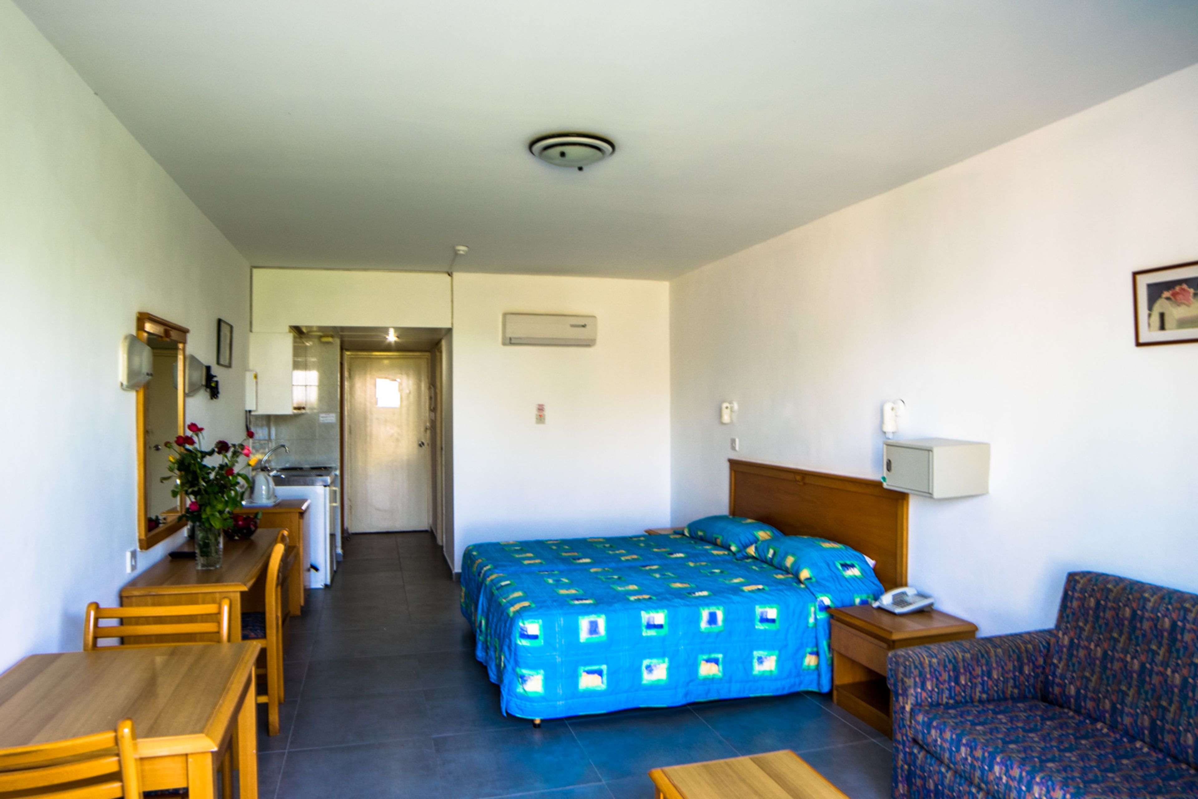 A hotel room with a bed, a sofa, a desk, and a small kitchenette.