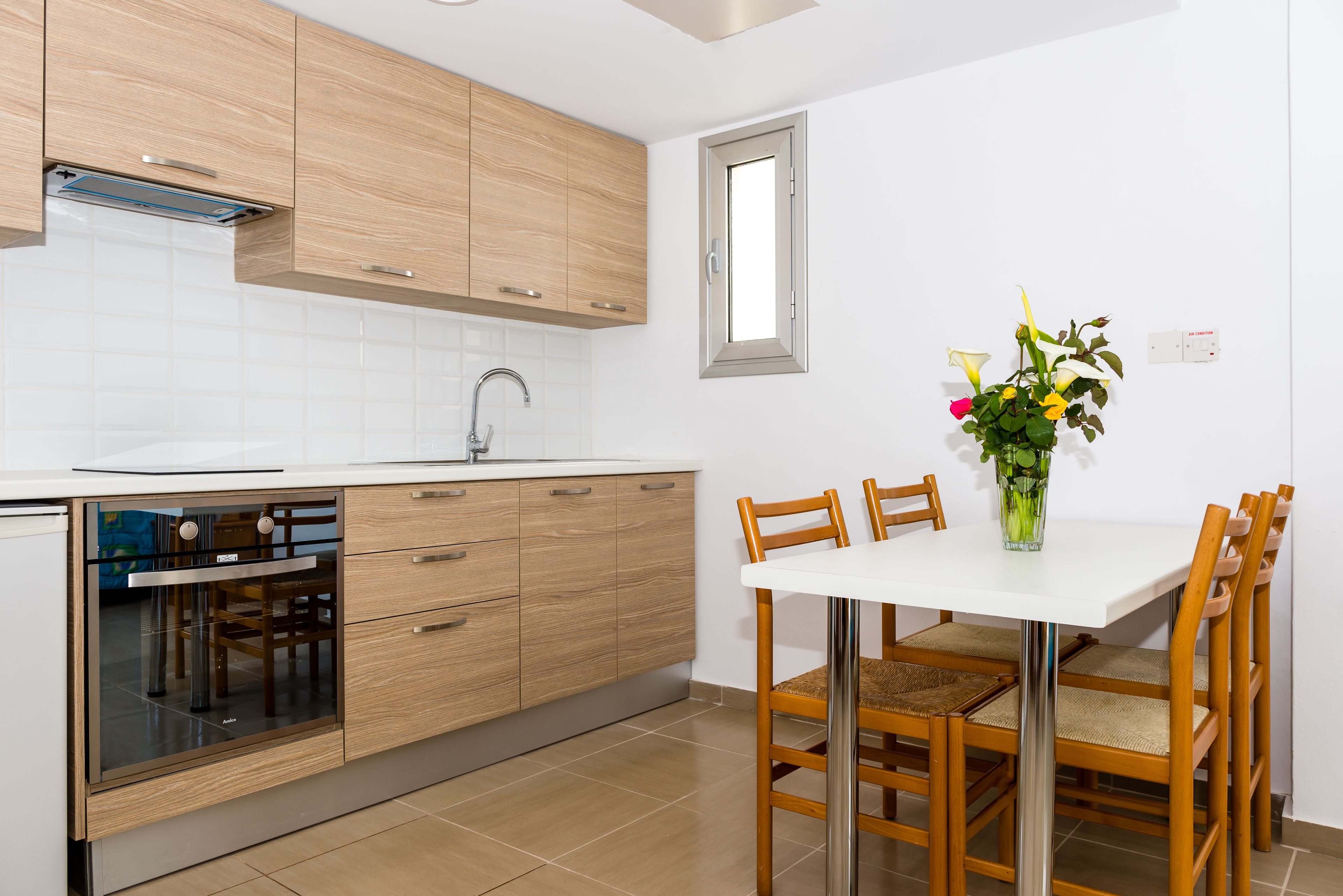 Une cuisine moderne avec des meubles en bois, un four encastré et un coin repas comprenant une table blanche et des chaises en bois.