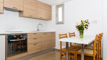 A modern kitchen with wooden cabinets, a built-in oven, and a dining area with a white table and wooden chairs.