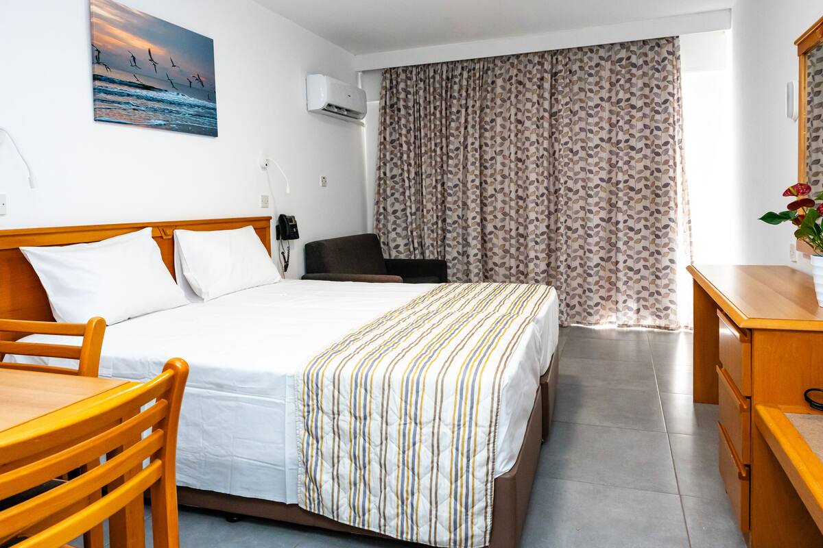 A hotel room with a bed, wooden furniture, a desk, a chair, a telephone, and a window with curtains.