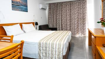 Habitación de hotel con cama, muebles de madera, escritorio, silla, teléfono y ventana con cortinas.