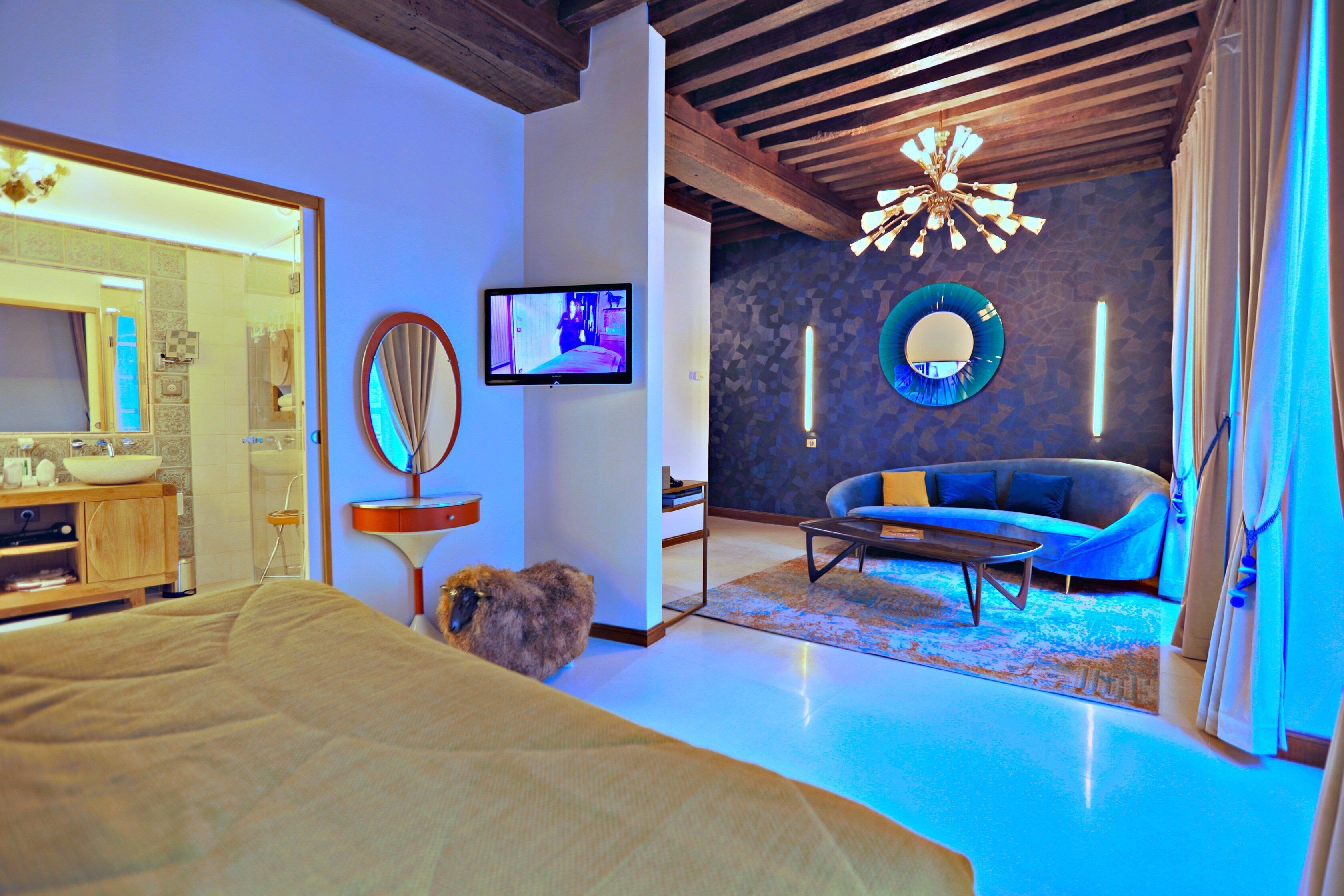 A modern hotel room with a bed, a television, a sofa, and a mirror.