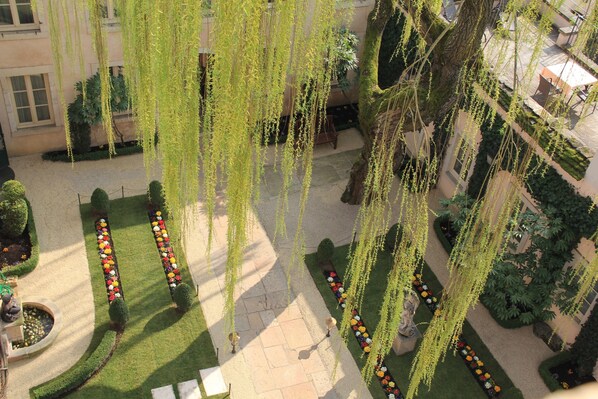 Un patio con plantas colgantes, setos perfectamente recortados y una estatua.