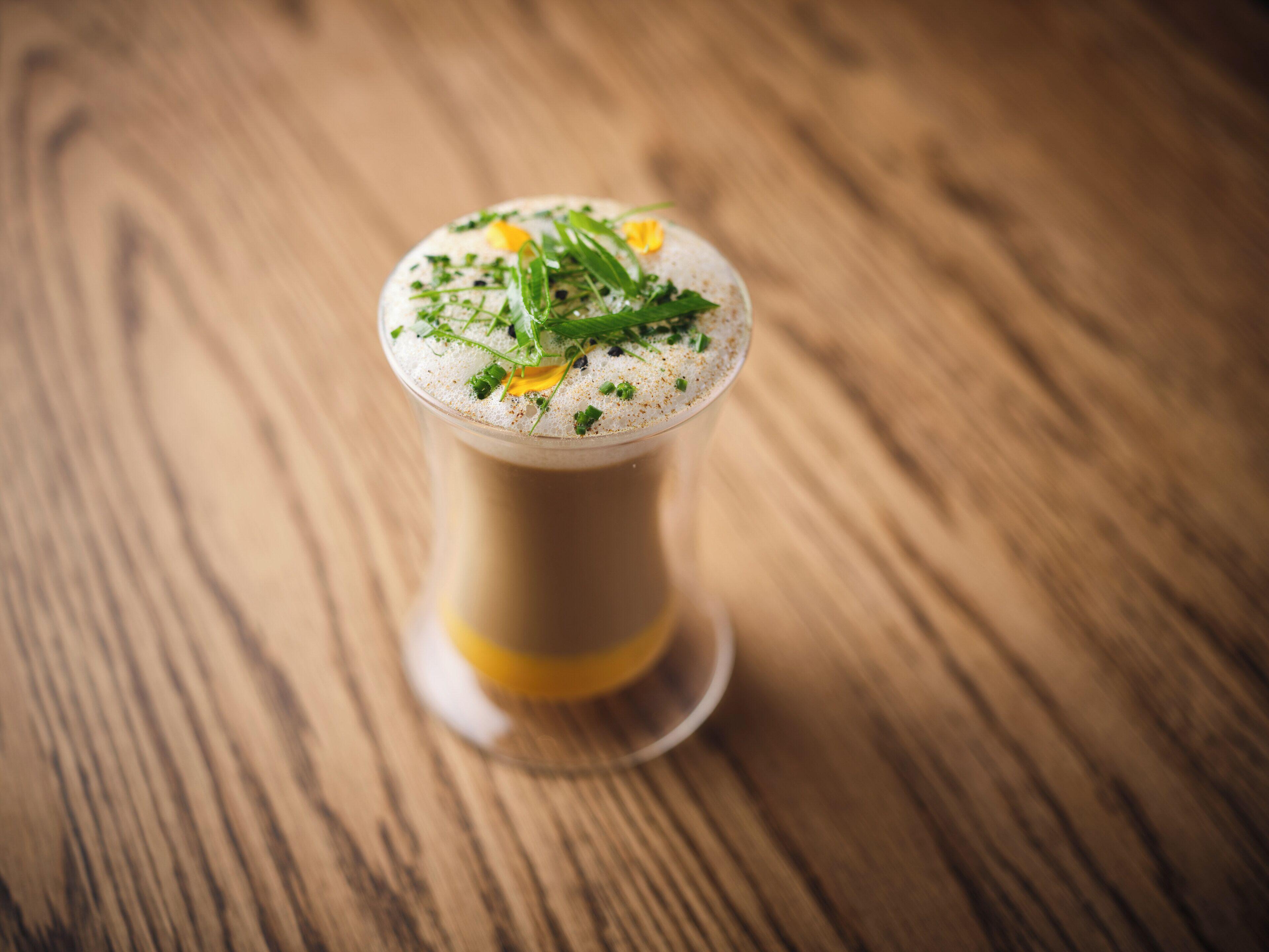 Un bicchiere di bevanda con schiuma, guarnito con erbe aromatiche, su un tavolo di legno.