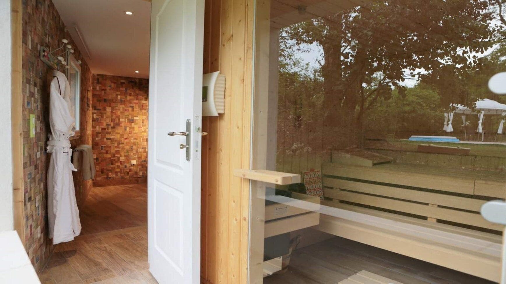 A wooden deck with a glass door leading to a room with a brick wall and a white robe hanging on the wall.