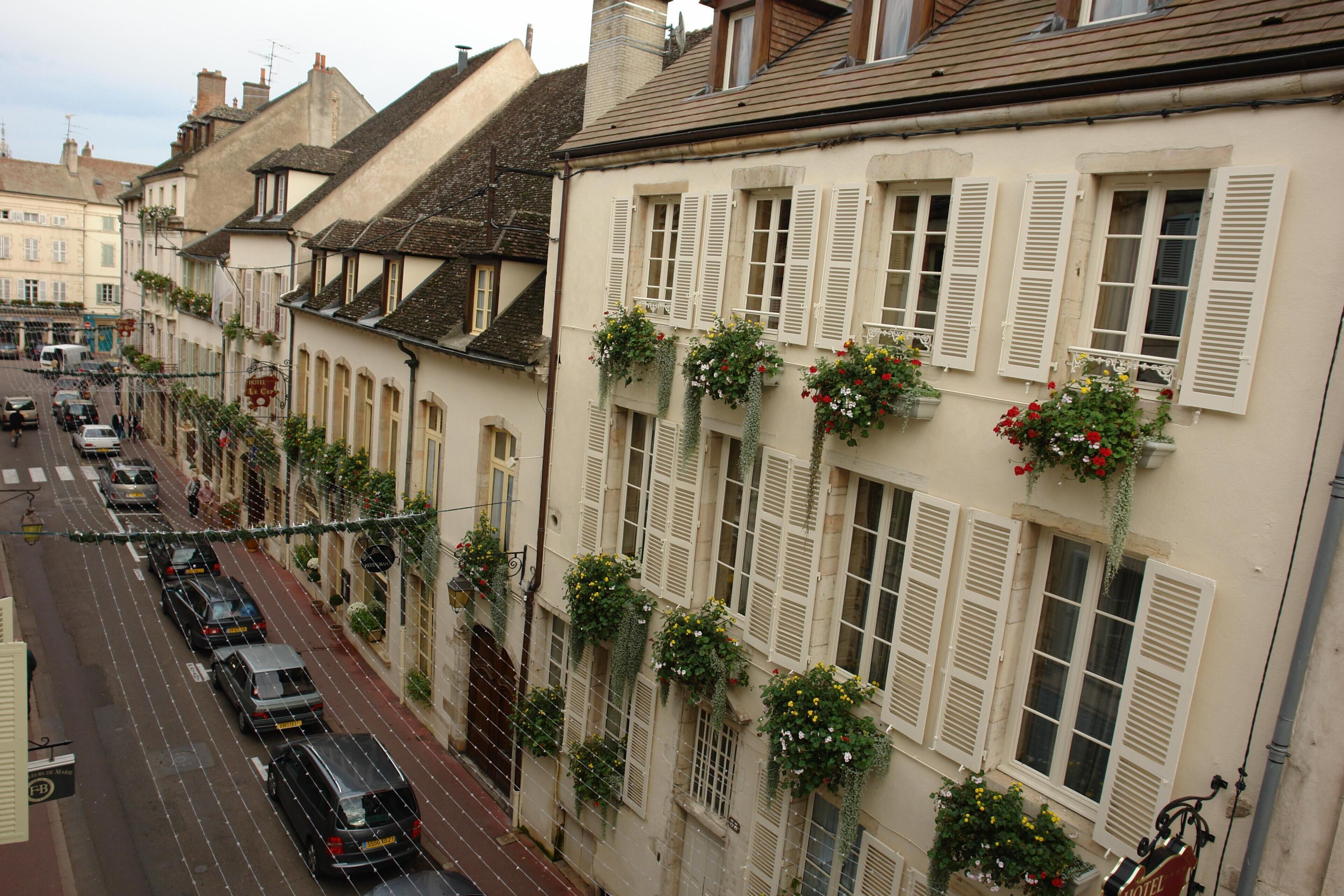 A street view of a row of buildings with white facades, shutters, and hanging flower baskets.