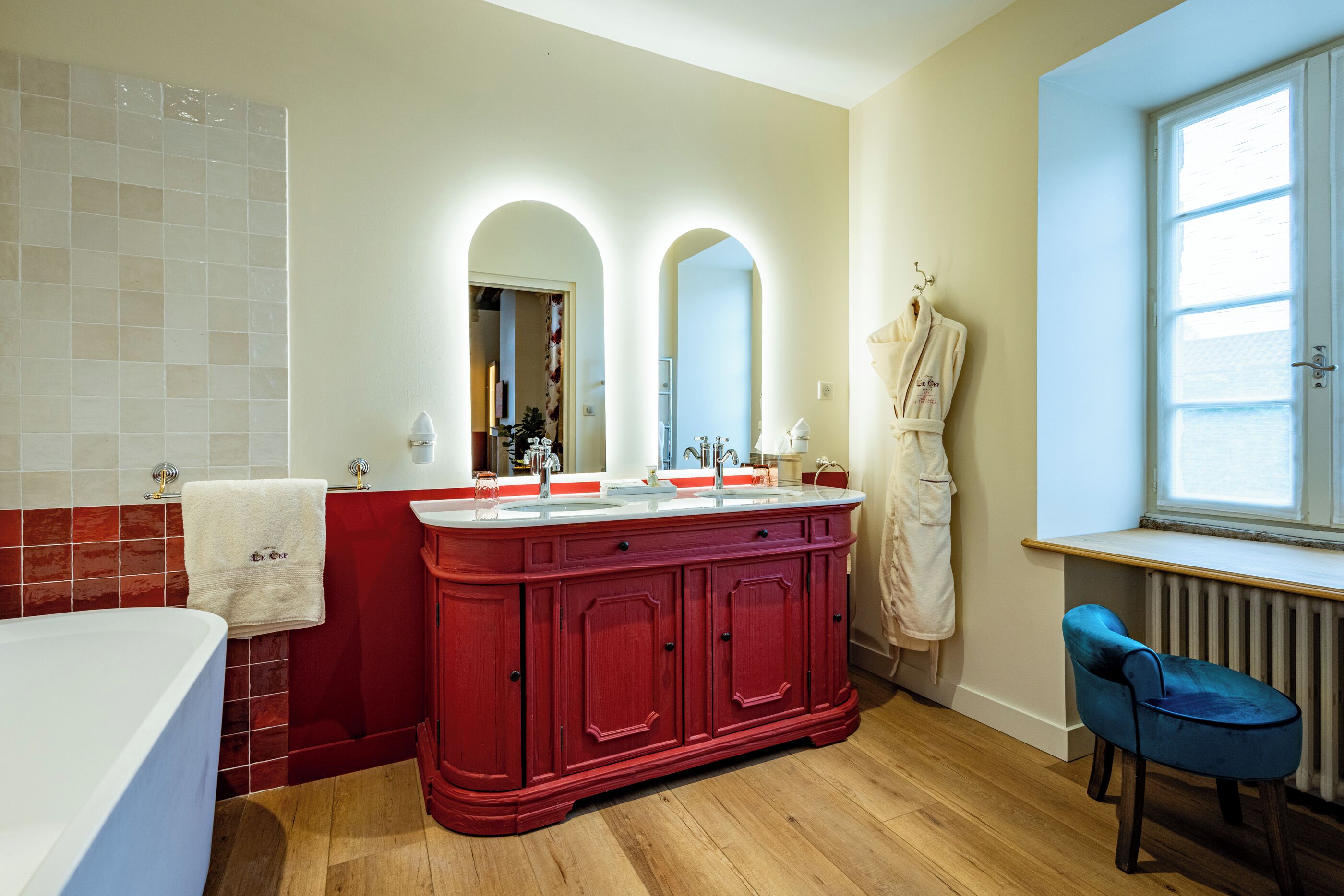 A bathroom with a red vanity, a white bathtub, and a blue chair.
