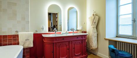 A bathroom with a red vanity, a white bathtub, and a blue chair.