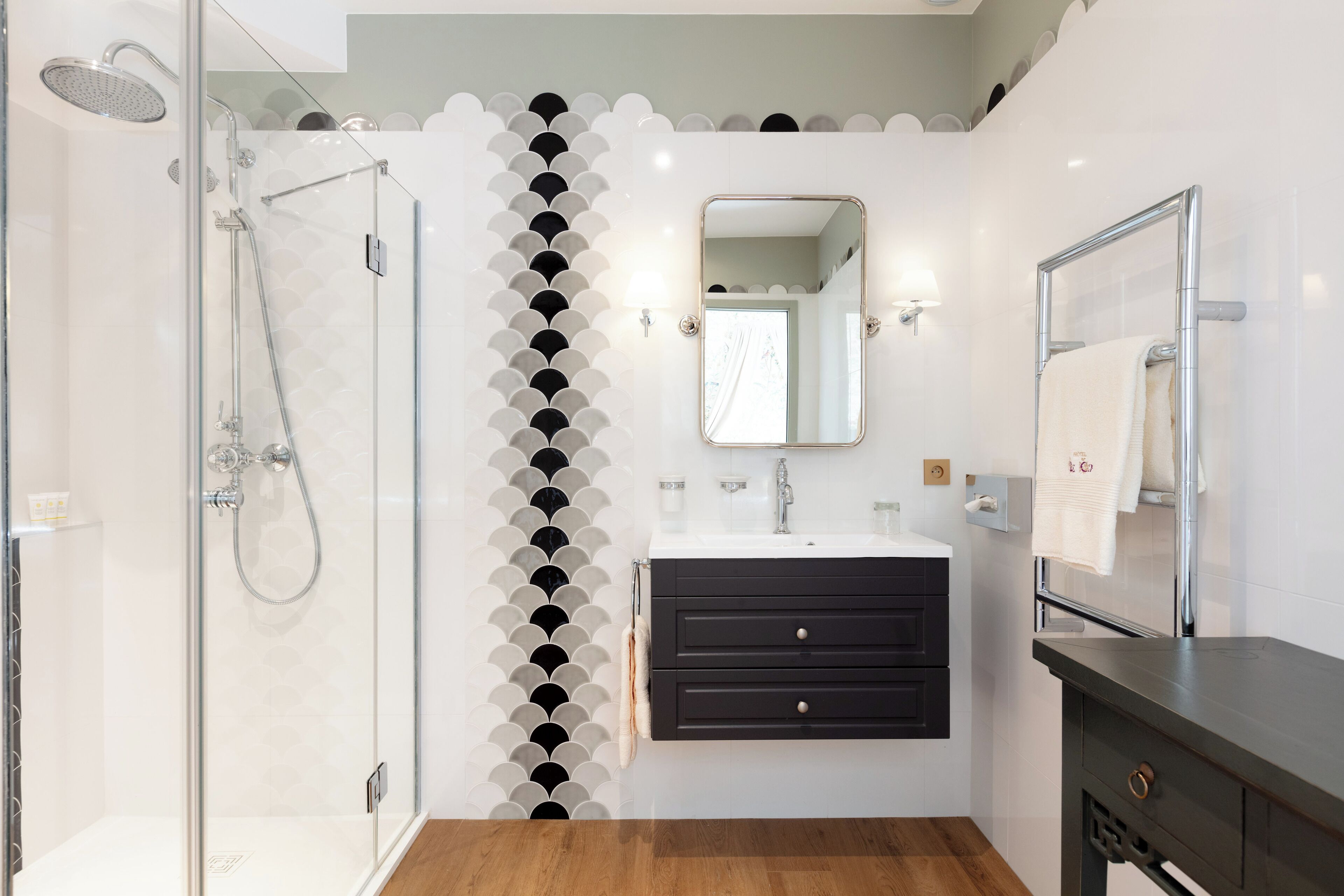 A modern bathroom with a glass shower enclosure, a black vanity with drawers, a mirror, and a towel rack.