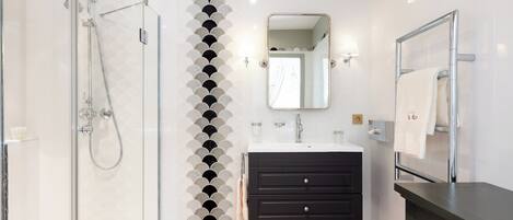 A modern bathroom with a glass shower enclosure, a black vanity with drawers, a mirror, and a towel rack.