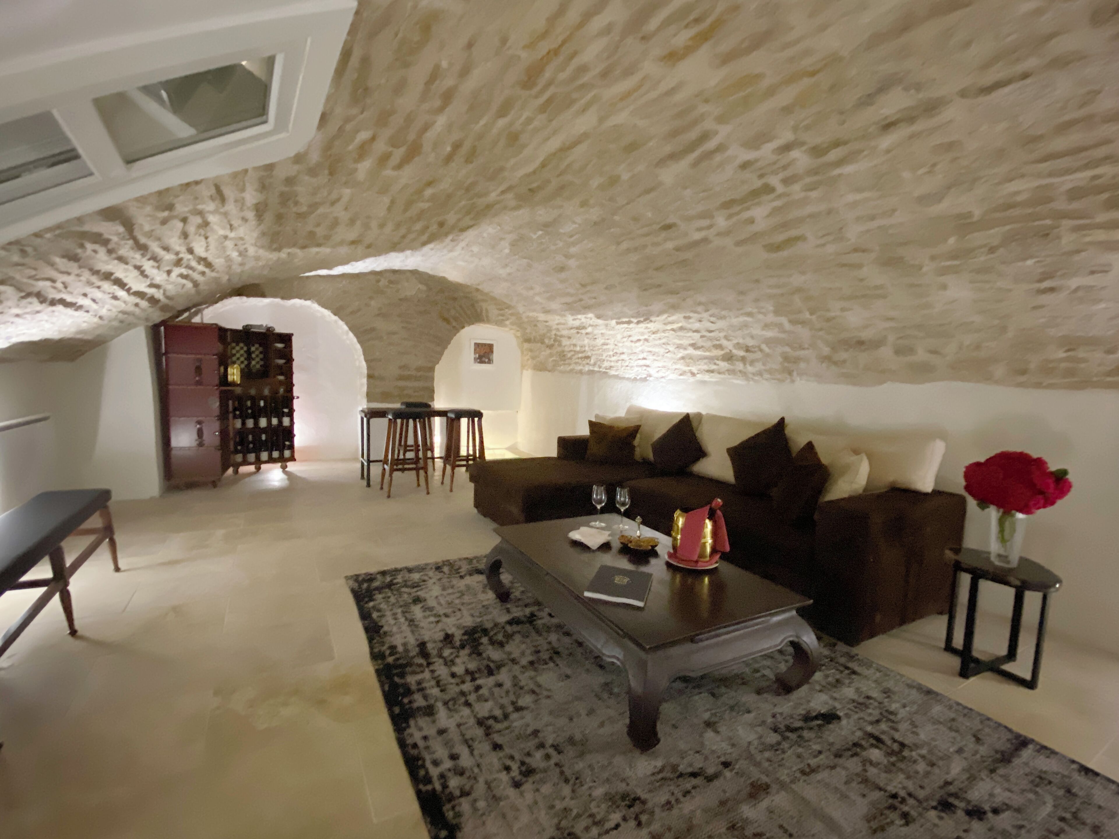 An attic room with a stone ceiling, a sofa, a coffee table, and a small table with a vase of flowers.