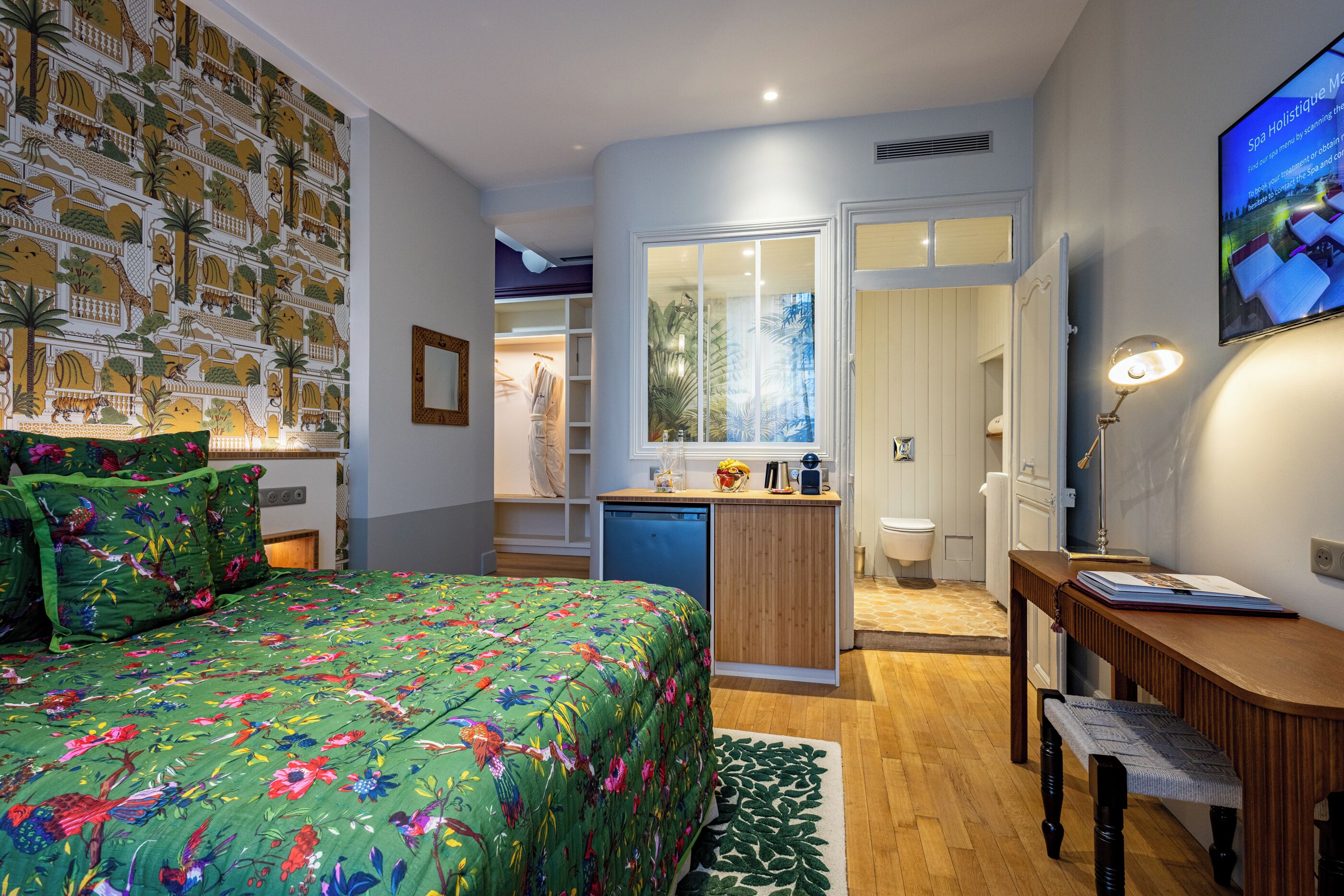 A bedroom with a bed, a desk, a chair, a small kitchenette, and a bathroom.