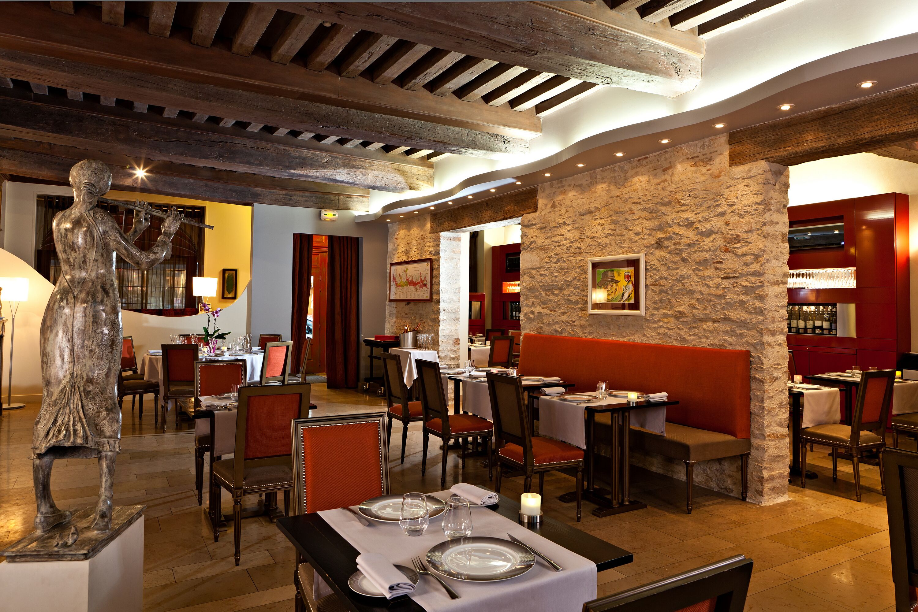 Un restaurante con paredes de piedra, vigas de madera y asientos acolchados rojos.