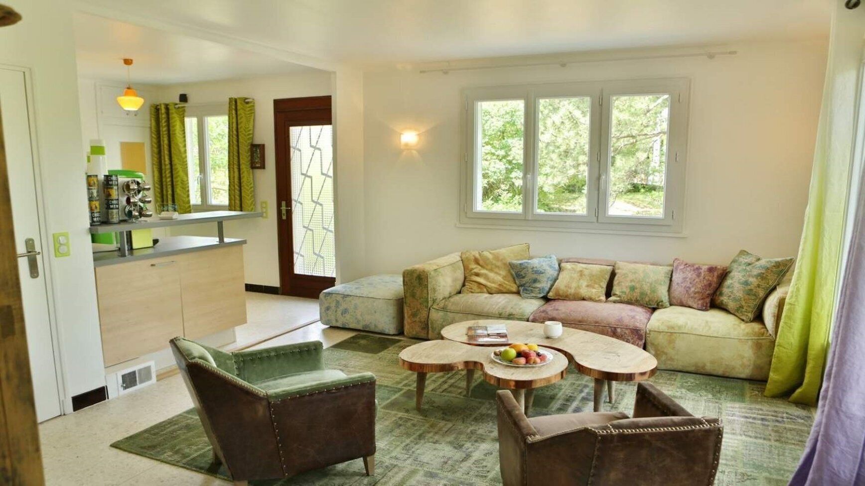A living room with a sofa, two armchairs, a coffee table, and a kitchen area with a refrigerator and cabinets.