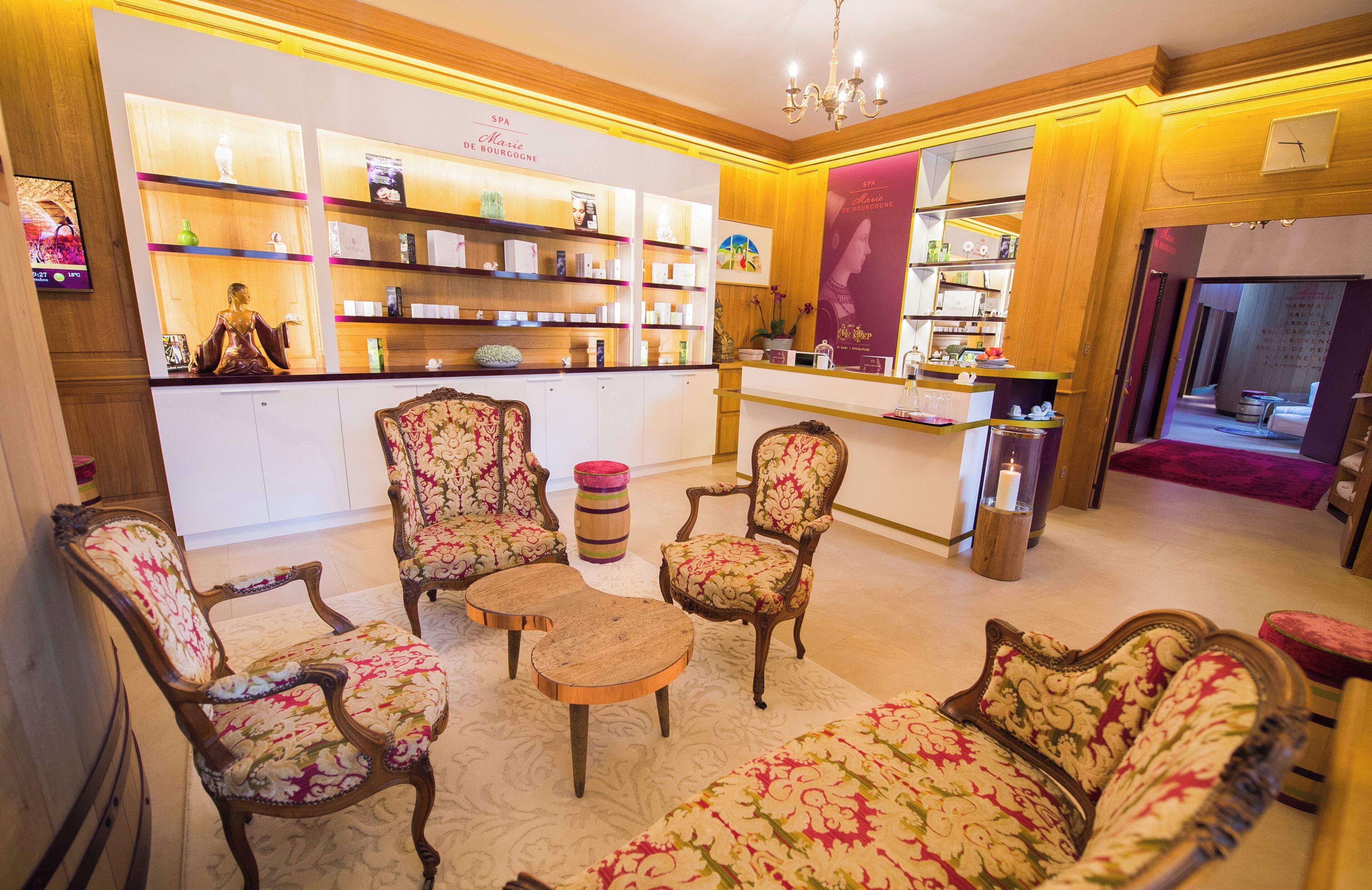 A hotel lobby with a reception desk, floral-patterned seating, and shelves with toiletries.