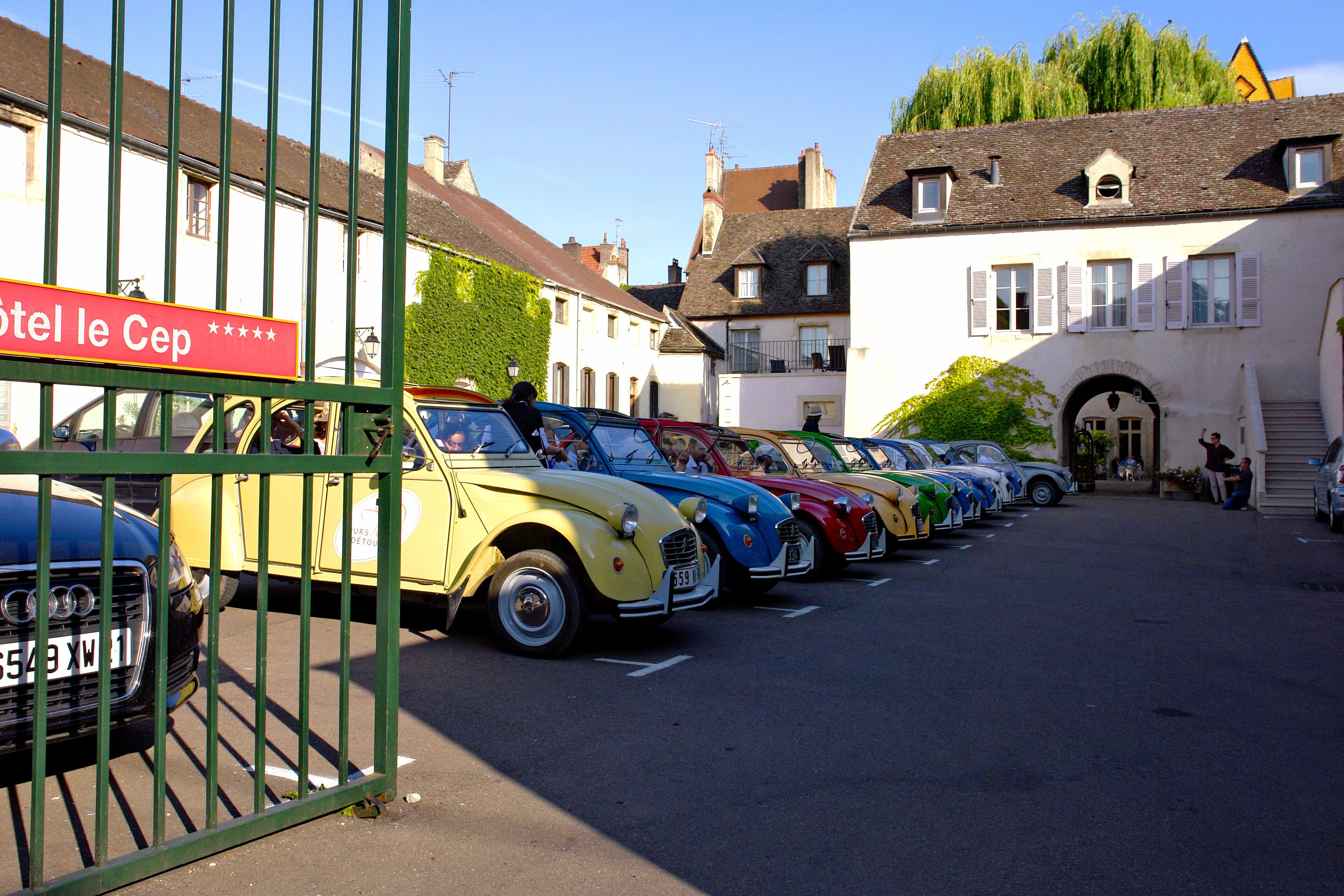 Eine Reihe klassischer Autos vor einem Gebäude mit der Aufschrift 'Hotel le Cep'.