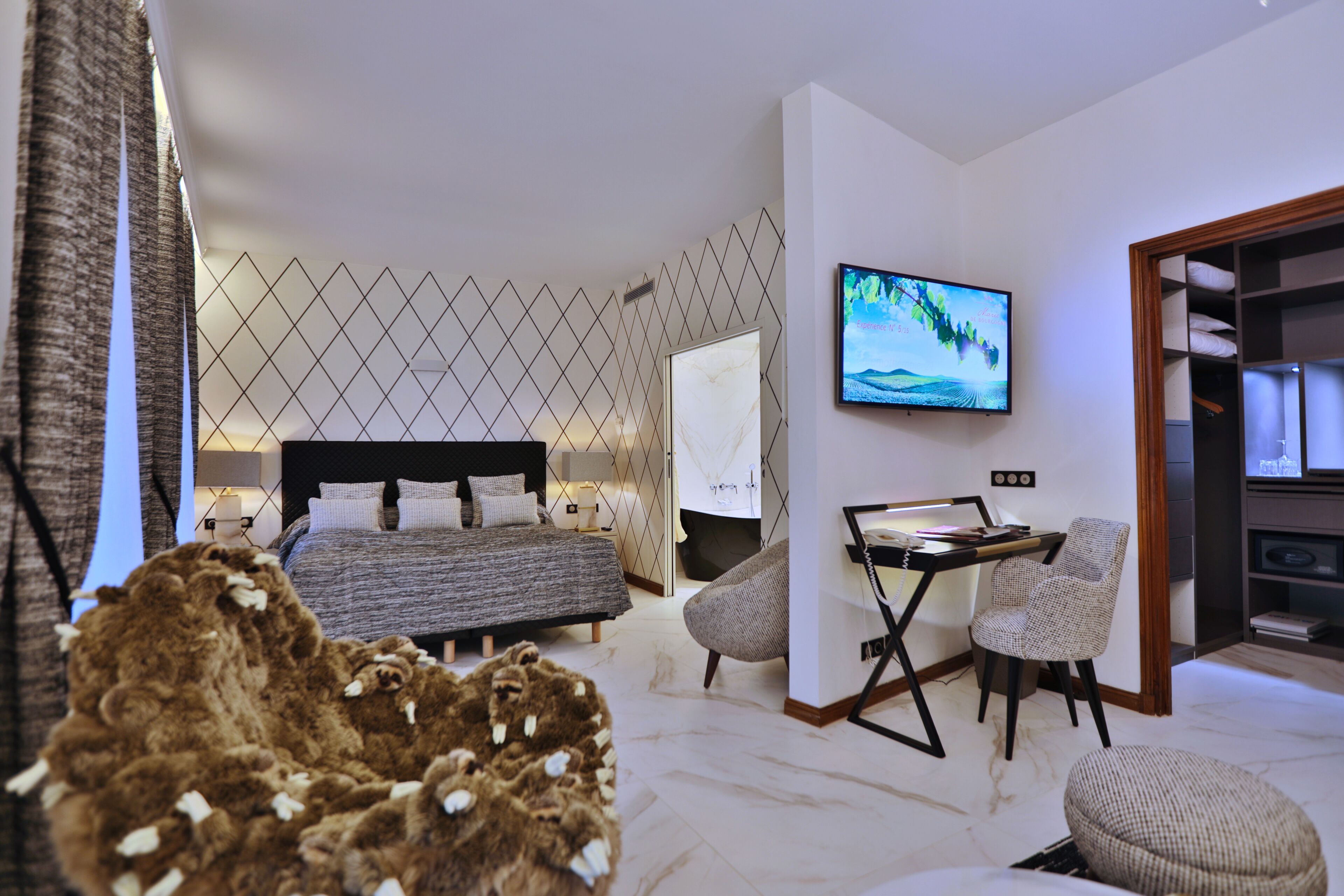 Ett modernt hotellrum med en välordnad säng, ett skrivbord med en stol, en tv och ett stort fönster.