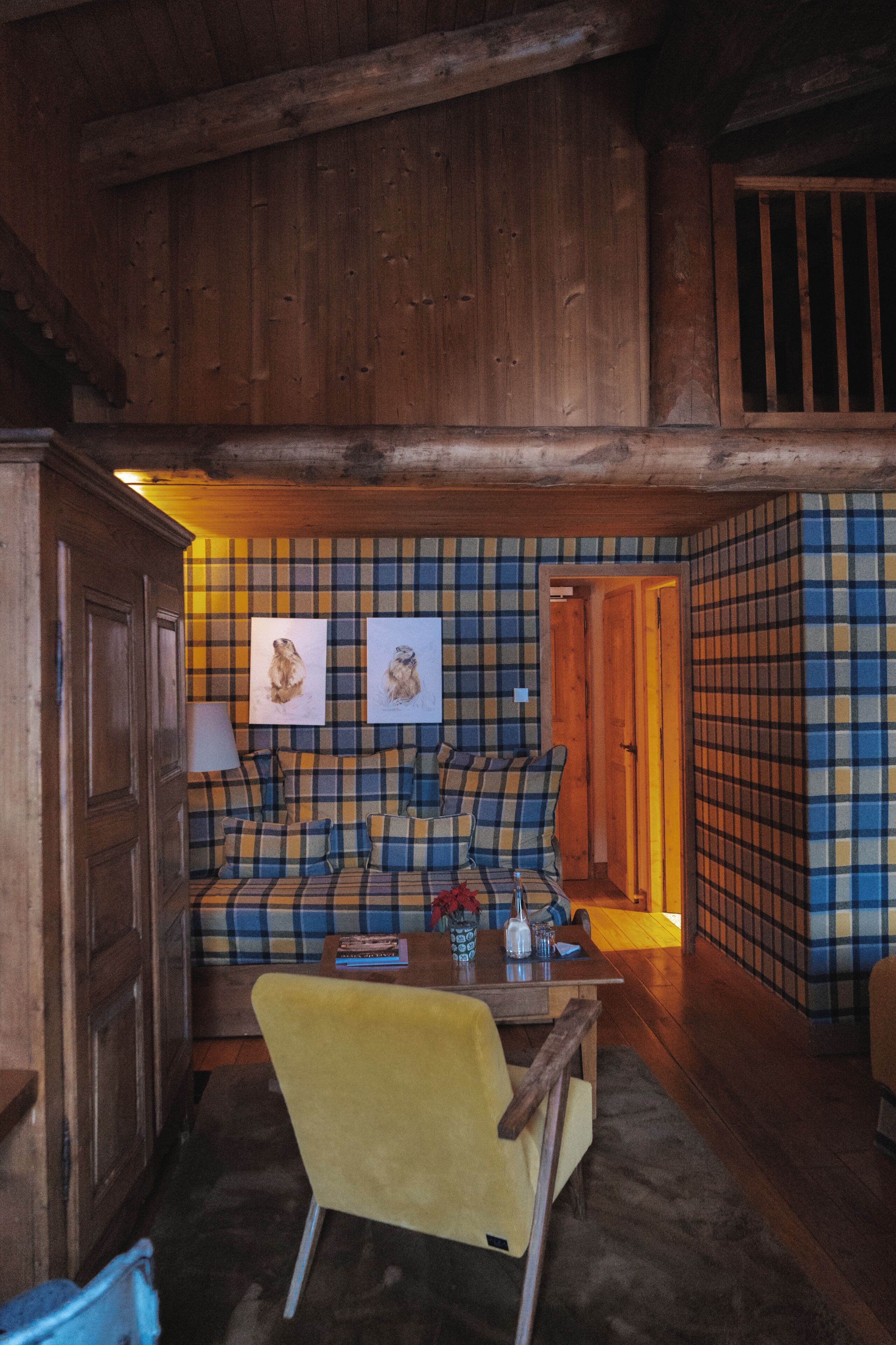 A cozy room with a plaid-patterned sofa, a yellow armchair, and wooden walls.