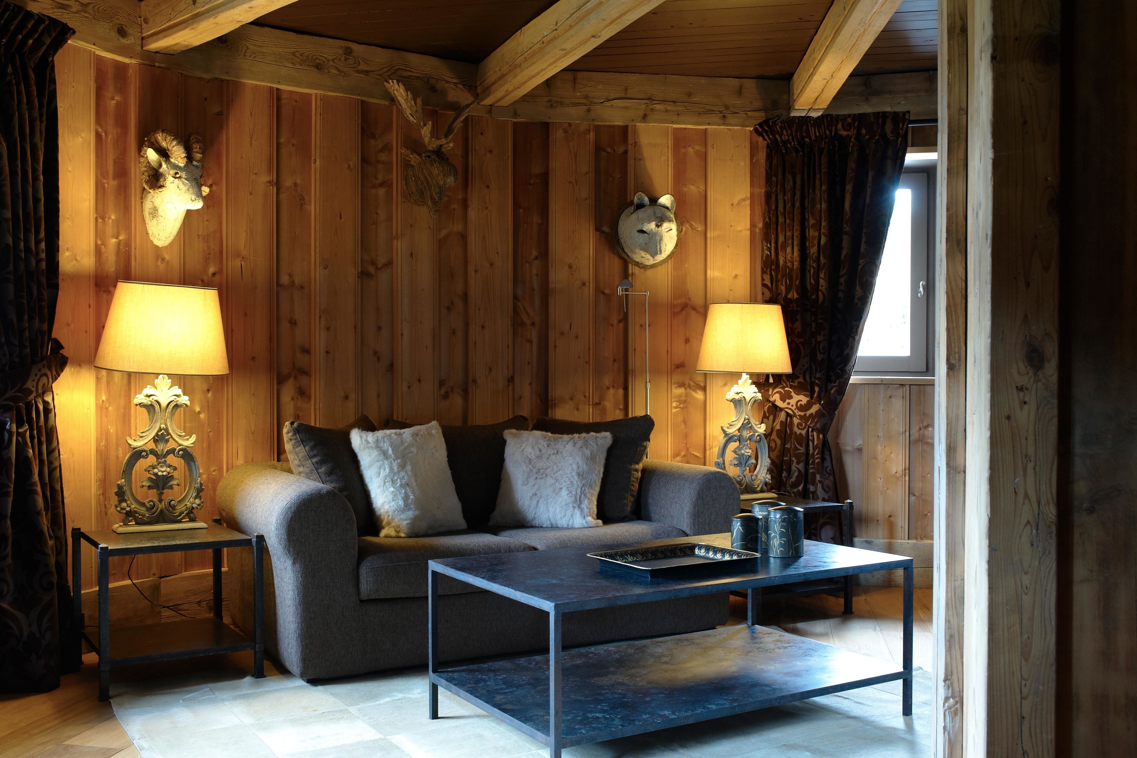 A cozy room with a sofa, two lamps, a coffee table, and wooden walls with mounted animal heads.
