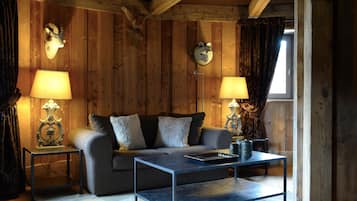 A cozy room with a sofa, two lamps, a coffee table, and wooden walls with mounted animal heads.