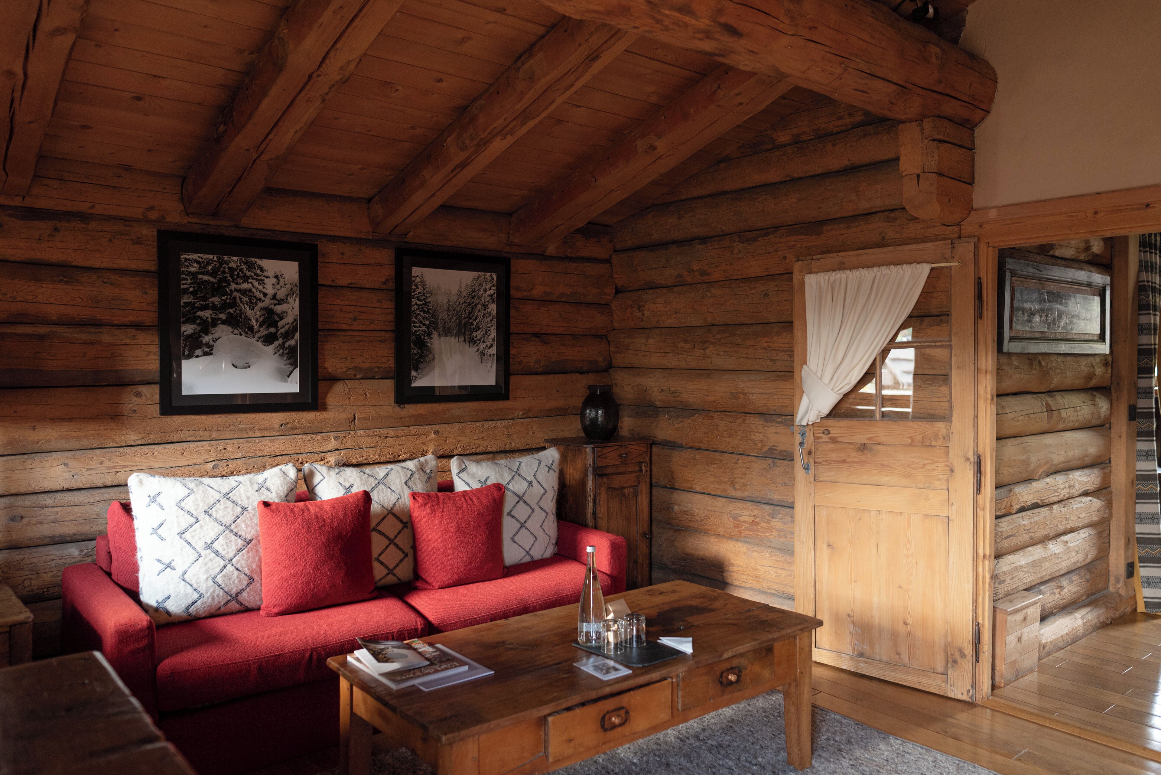 A log cabin interior with a red sofa, wooden coffee table, and framed pictures on the walls.