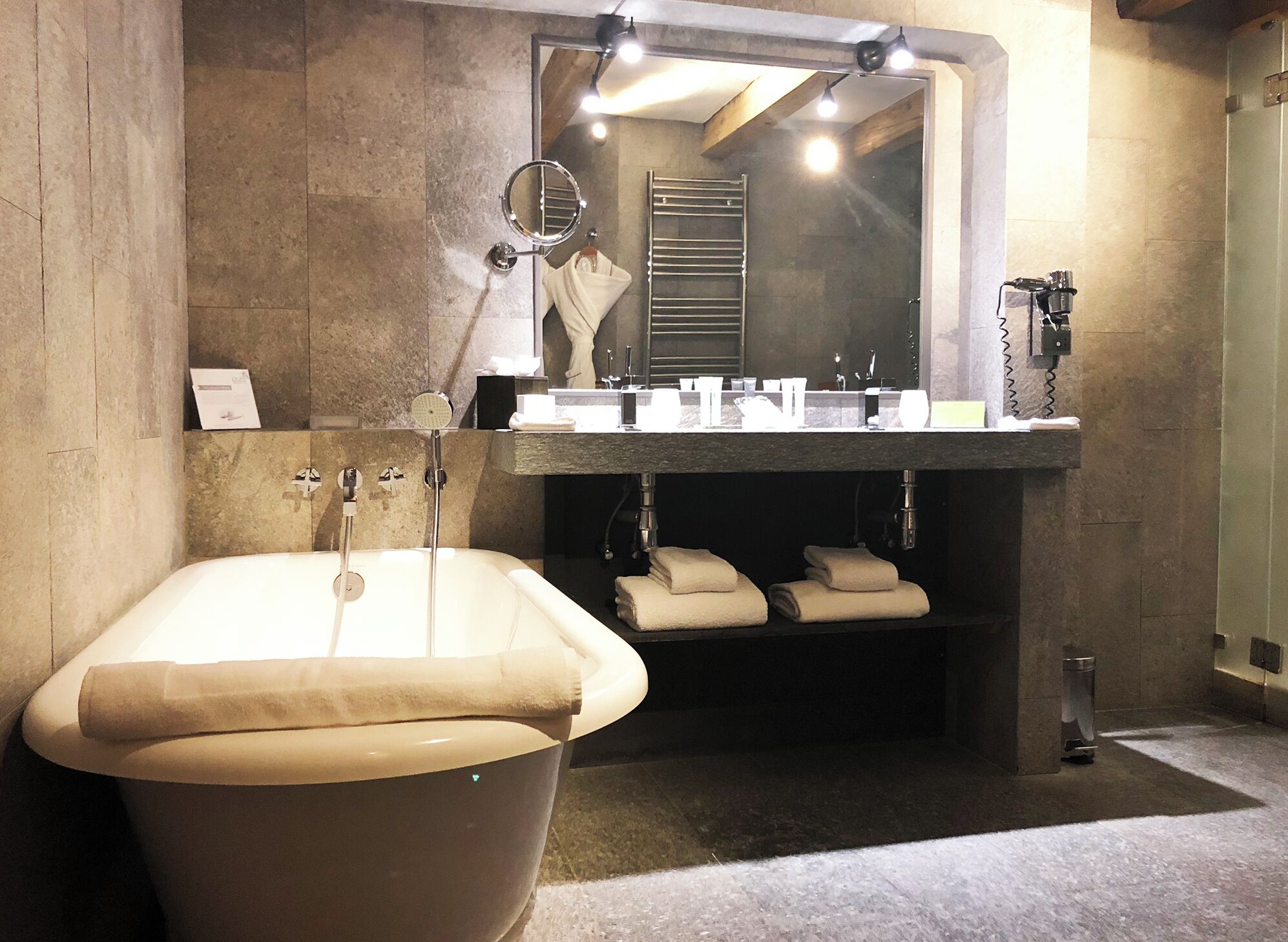 Un baño moderno con una bañera independiente, un espejo grande y un tocador con lavamanos y perchero.