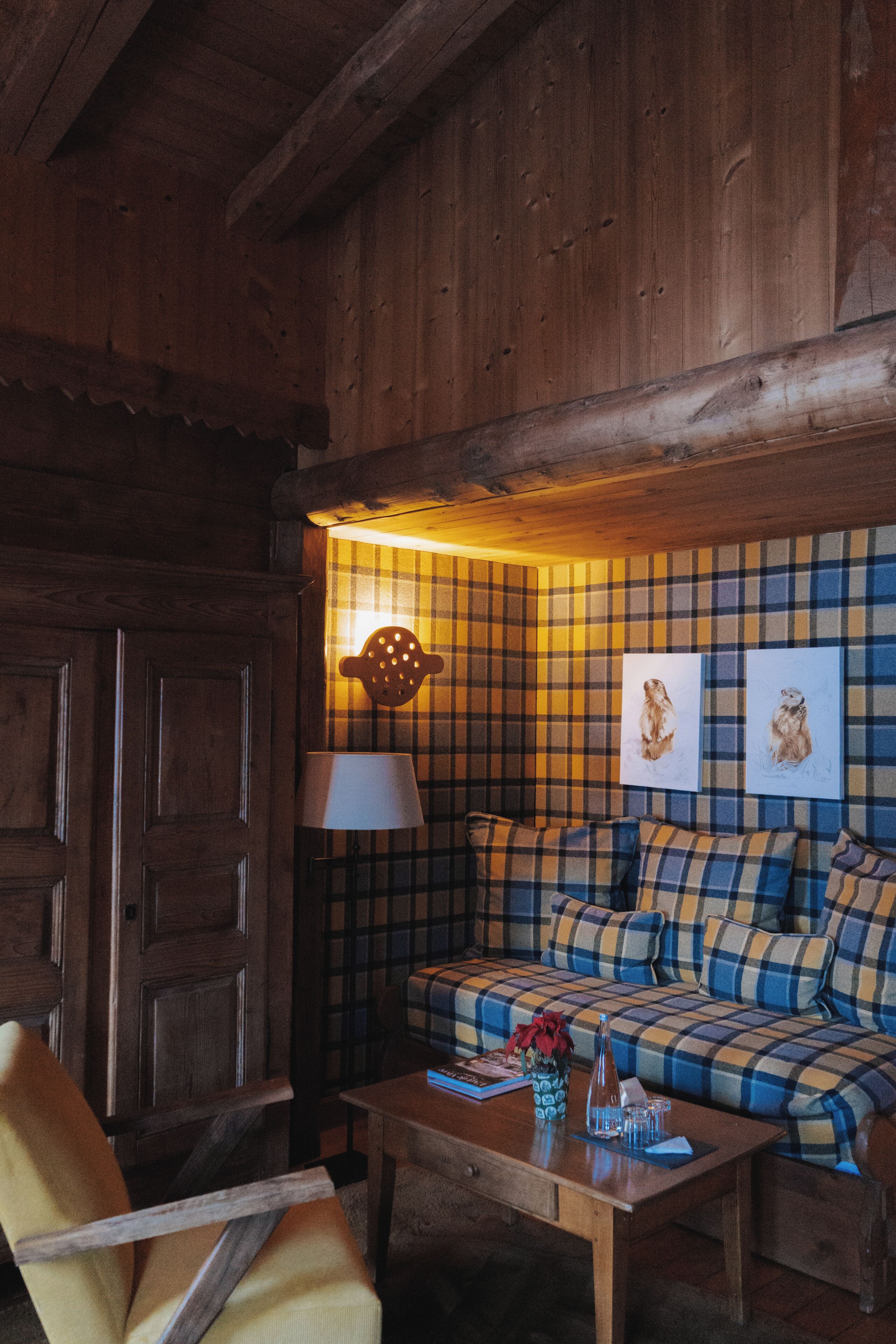 Un accogliente interno di una baita con un divano a motivi tartan, un tavolo di legno e una lampada.